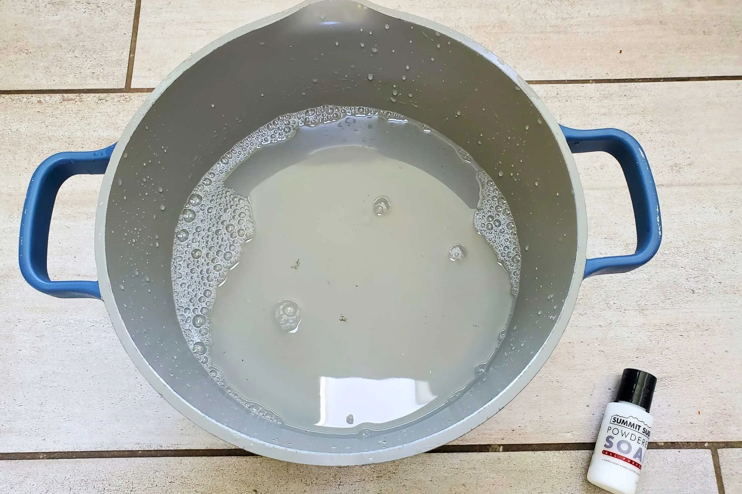 A small bottle of Summit Suds lays next to a pot of soapy water. The water is only slightly foamy-looking.