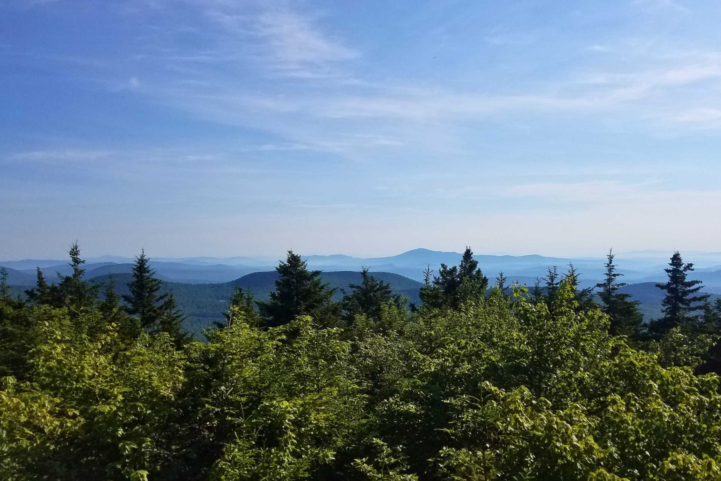 Beautiful  view from the Monadnock Sunapee Greenway with bright green trees in the foreground and hills and mountains off in the distance
