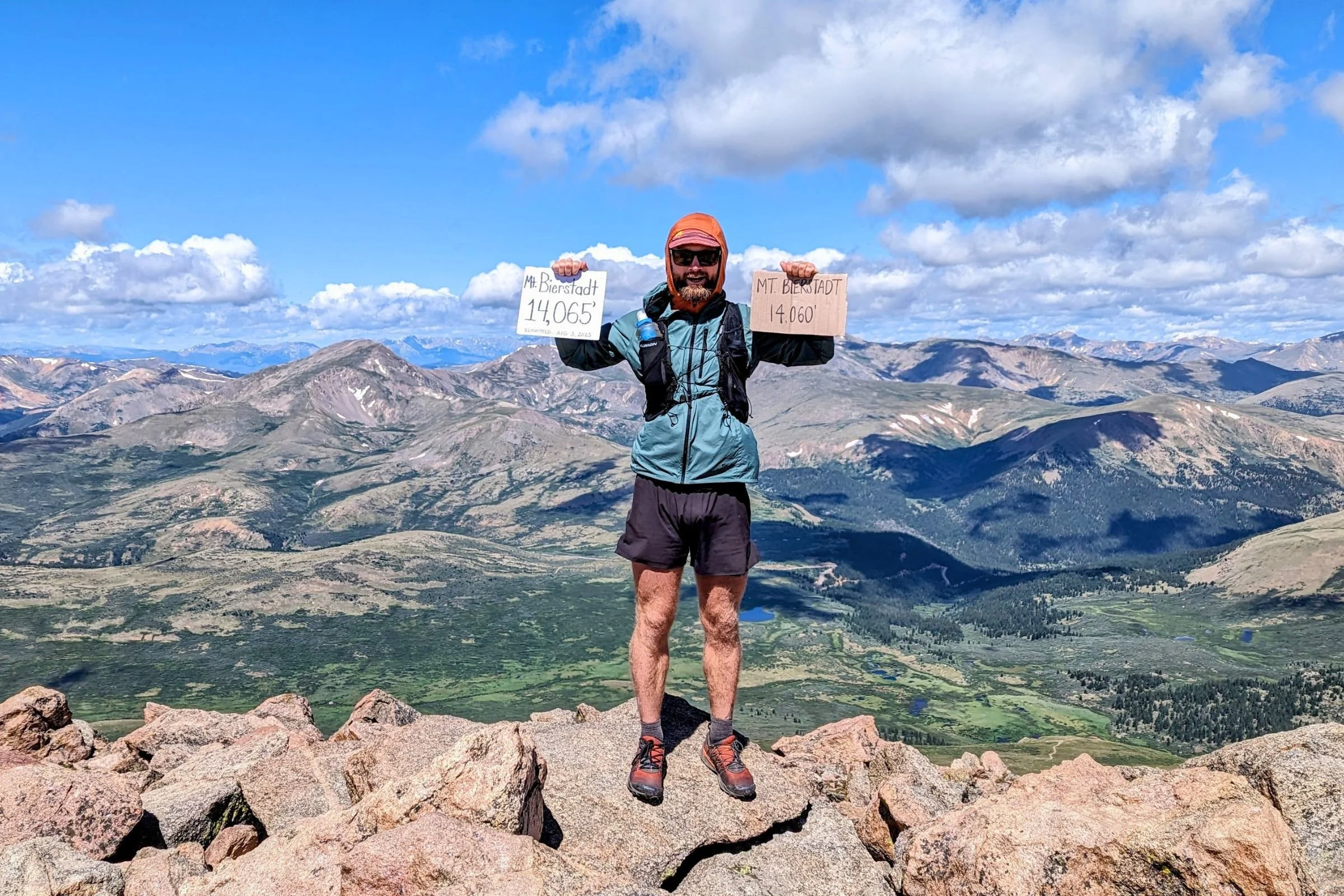 Man in Patagonia Strider Pro shorts holding up a sign on top of a mountain.