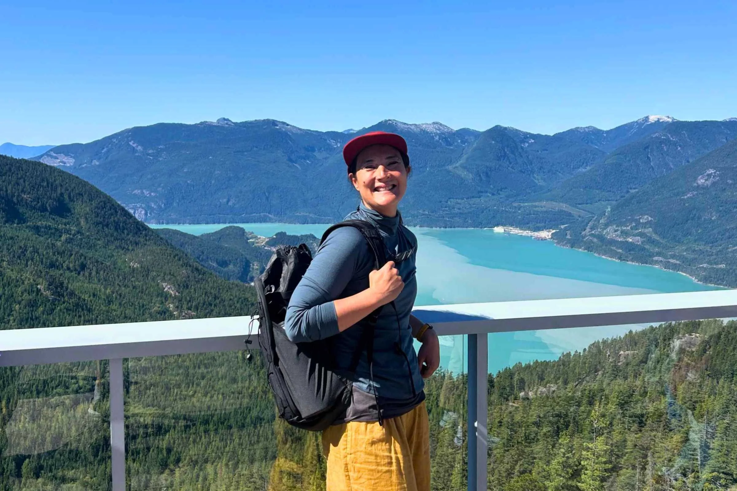 ULA Ultra Dragonfly 30L Adventure Travel Backpack worn by a woman standing on a wooden railing beside a lake.