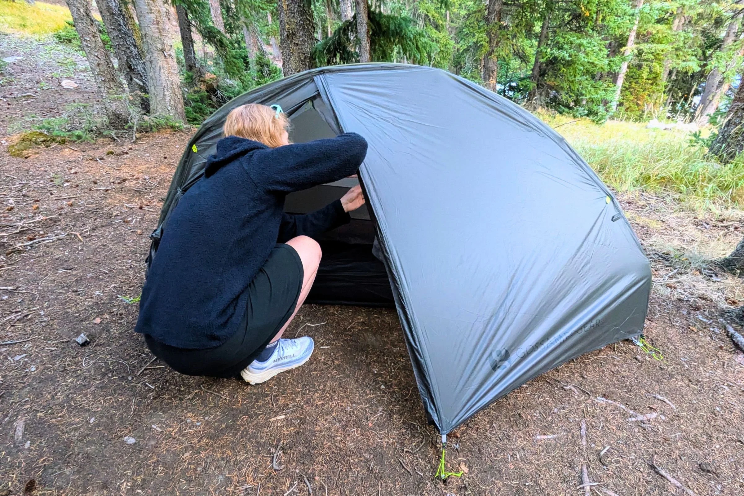 A tester crouches in the vestibule of the Gossamer Gear The Free at a forest campsite