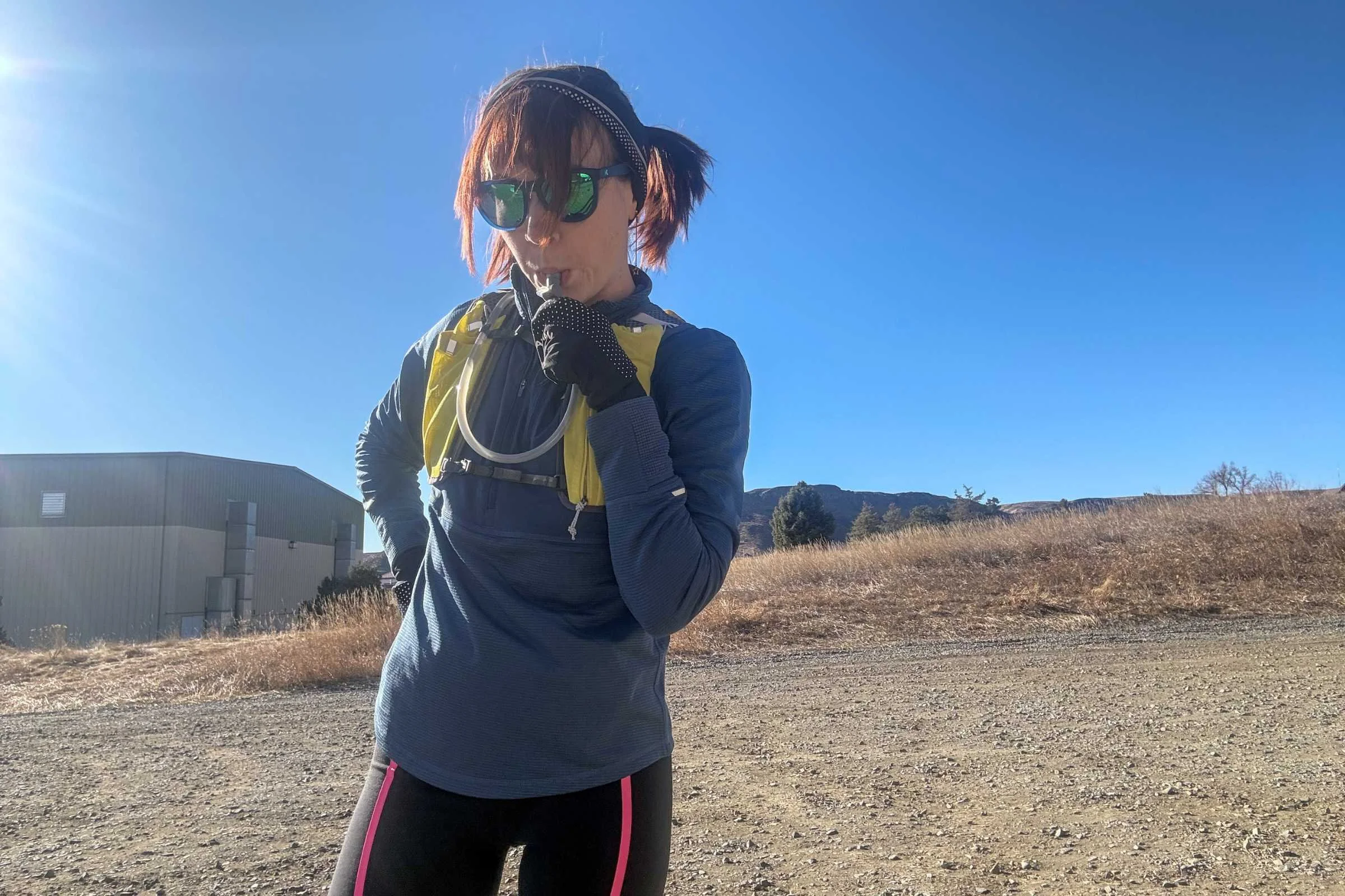 Woman drinking from a hydration bladder while wearing REI Co-op Swiftland Grid Running Shirt and Swiftland 5 Hydration Vest.