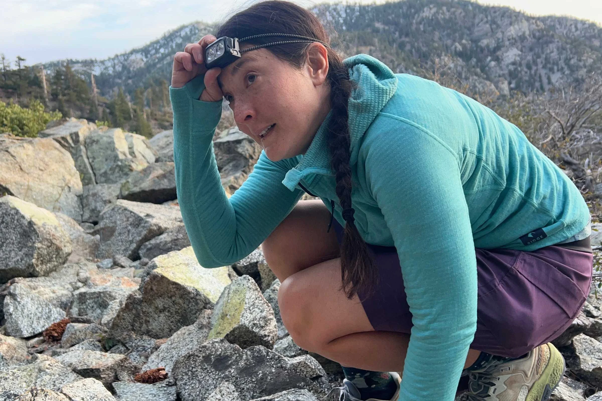 Hiker adjusting the Nitecore NU25 MCT headlamp while crouched on a rocky alpine trail.