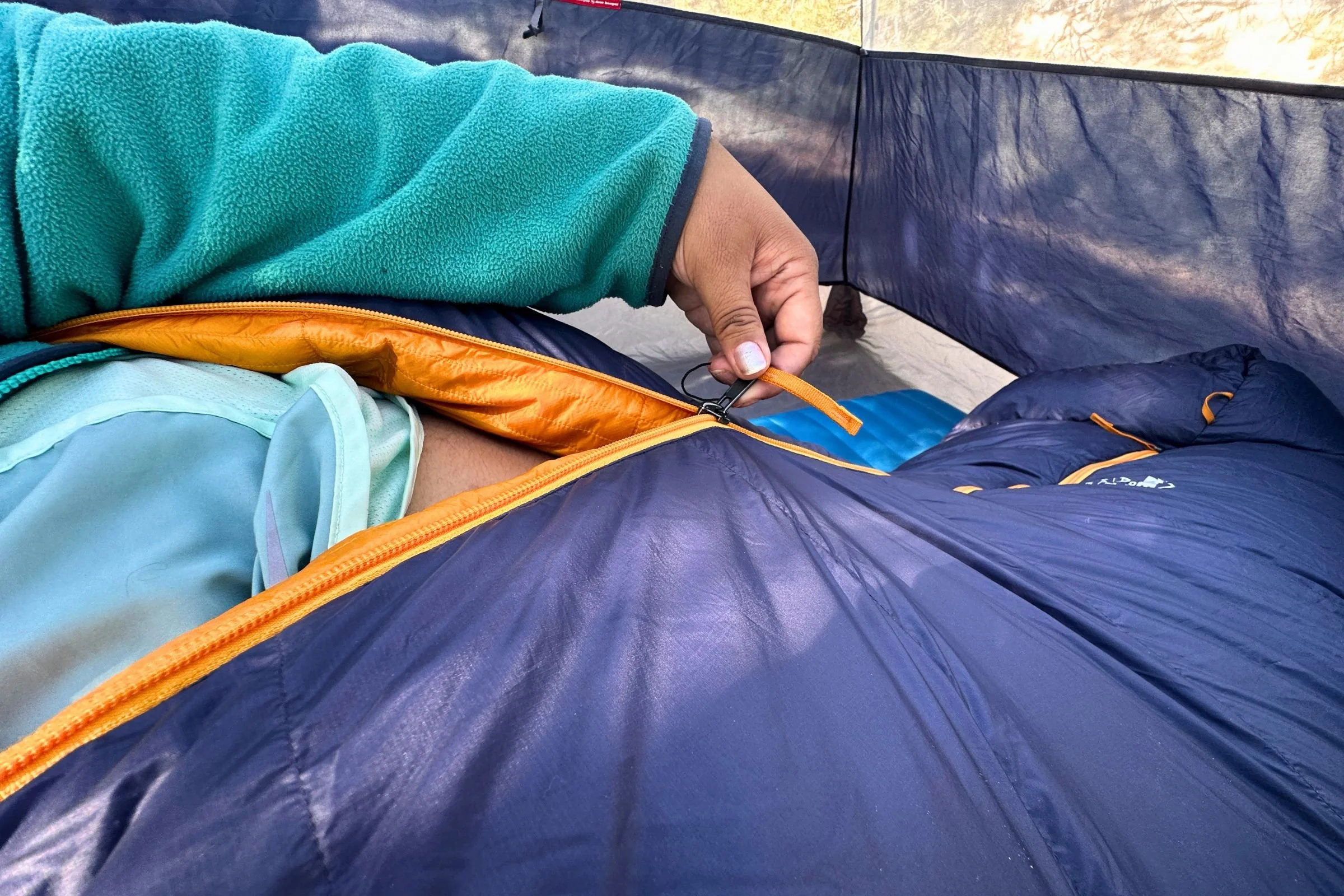 Tester unzipping the REI Co-op Magma 30 sleeping bag while lying inside it.