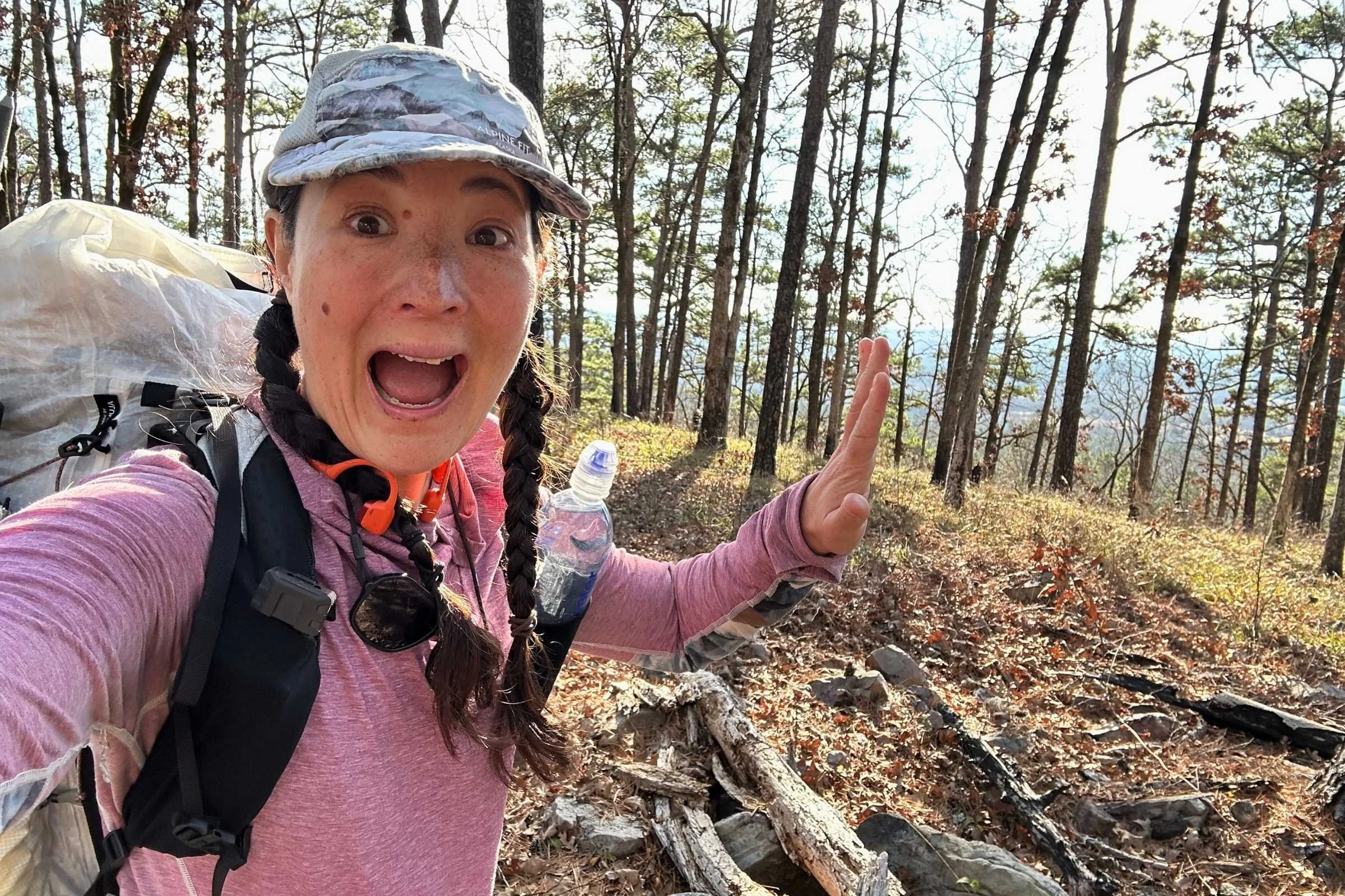 Treeline Review founder Liz Thomas taking an enthusiastic selfie on the Ouachita Trail, wearing some of her favorite thru-hiking gear