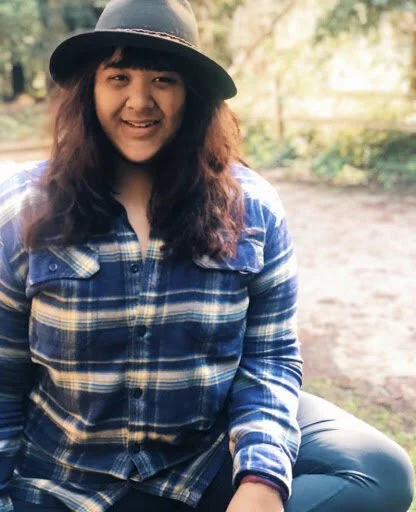 headshot of the author wearing a plaid shirt outdoors