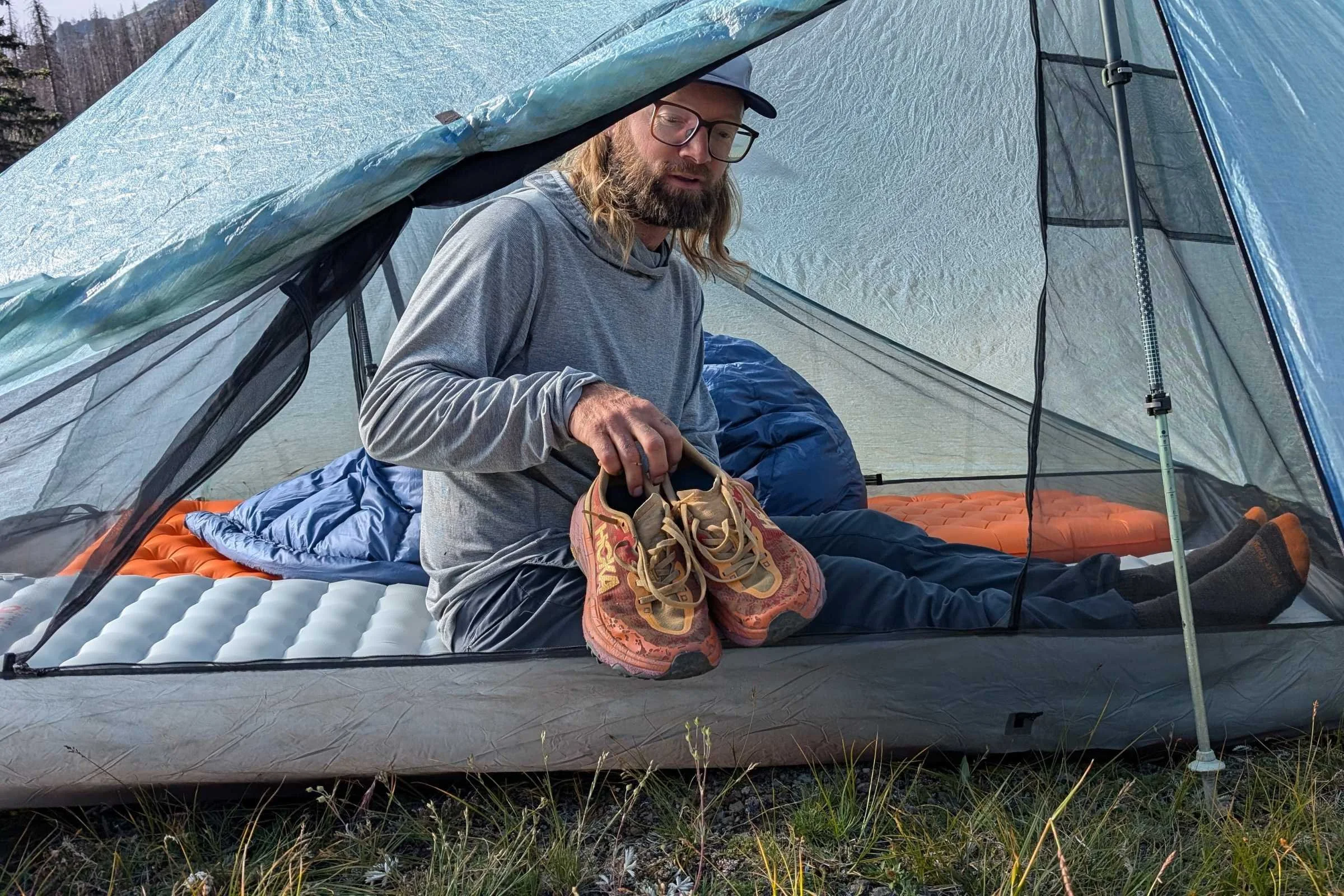 Man sitting inside a tent placing his Hoka Speedgoat 6 trail running shoes into the vestibule