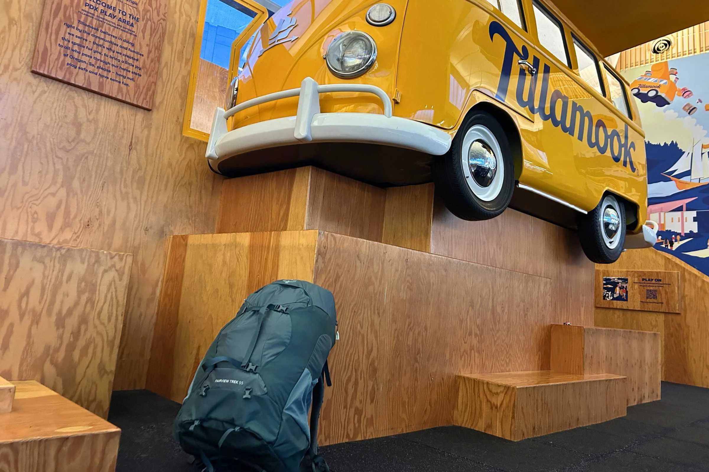 Osprey Fairview Trek 55 Travel Pack with Yellow bus displayed on a wooden platform.