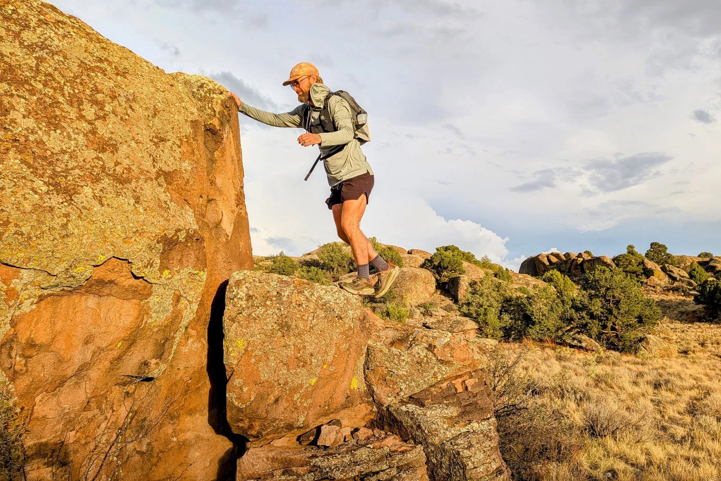 A man wearing the Altra Olympus 7 climbs a rock in a desert landscape.