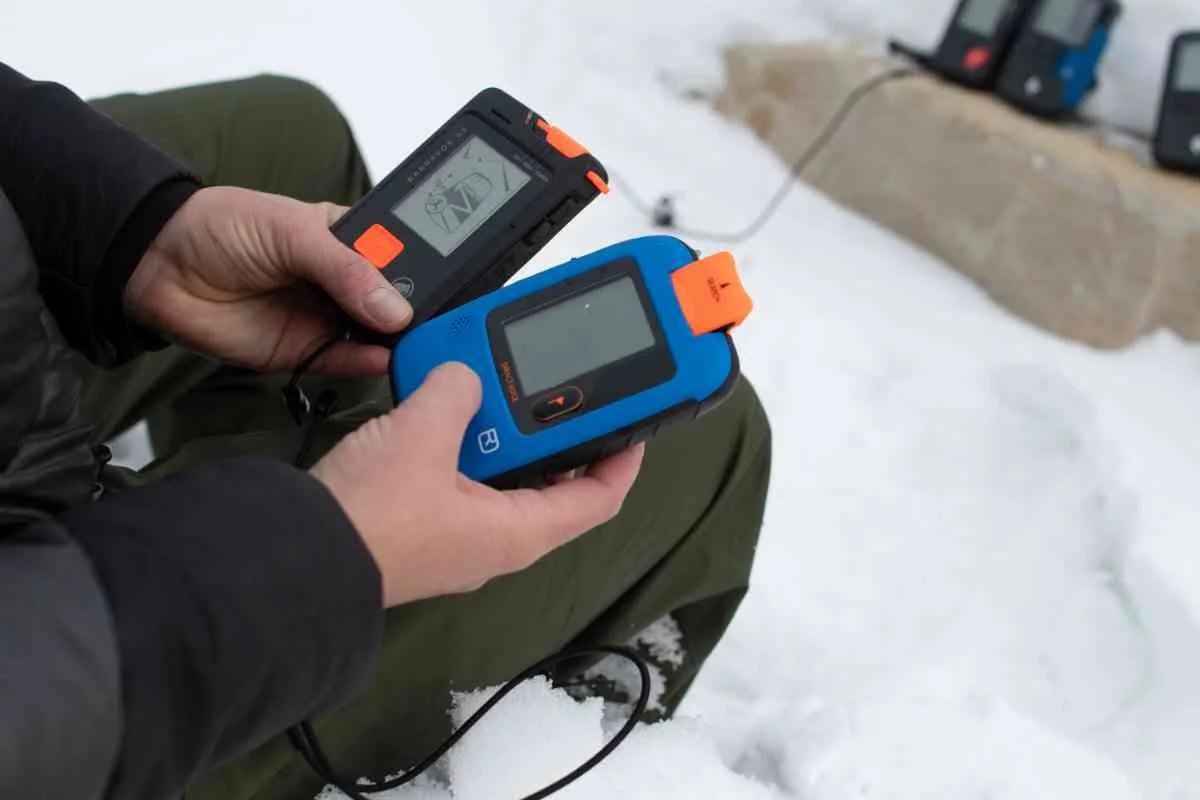 Person holding 2 avalanche beacons in the snow