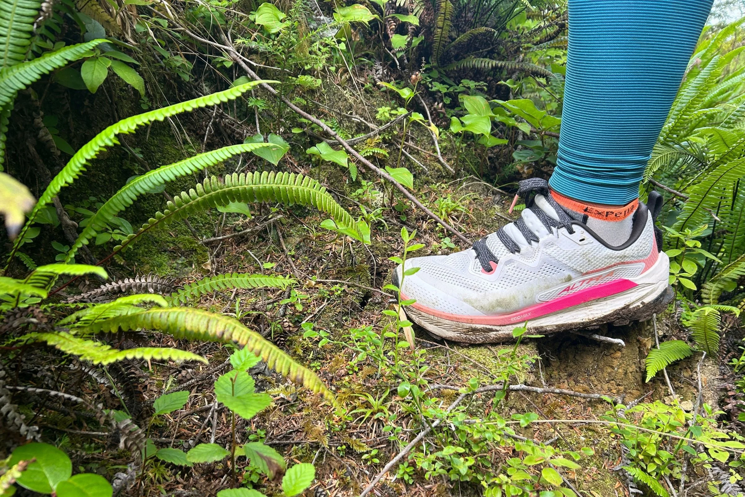 A person wearing the Altra Olympus 7 stands among trees in a wooded setting.