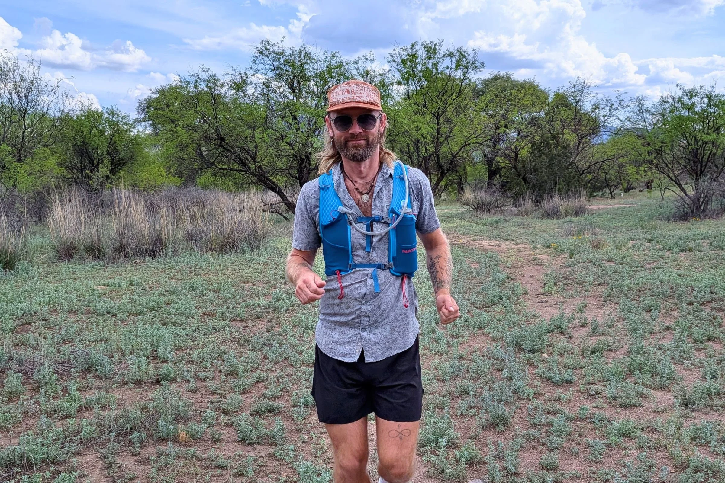 Man running along a dirt road while wearing a Nathan VaporAir pack, with a landscape in the background.