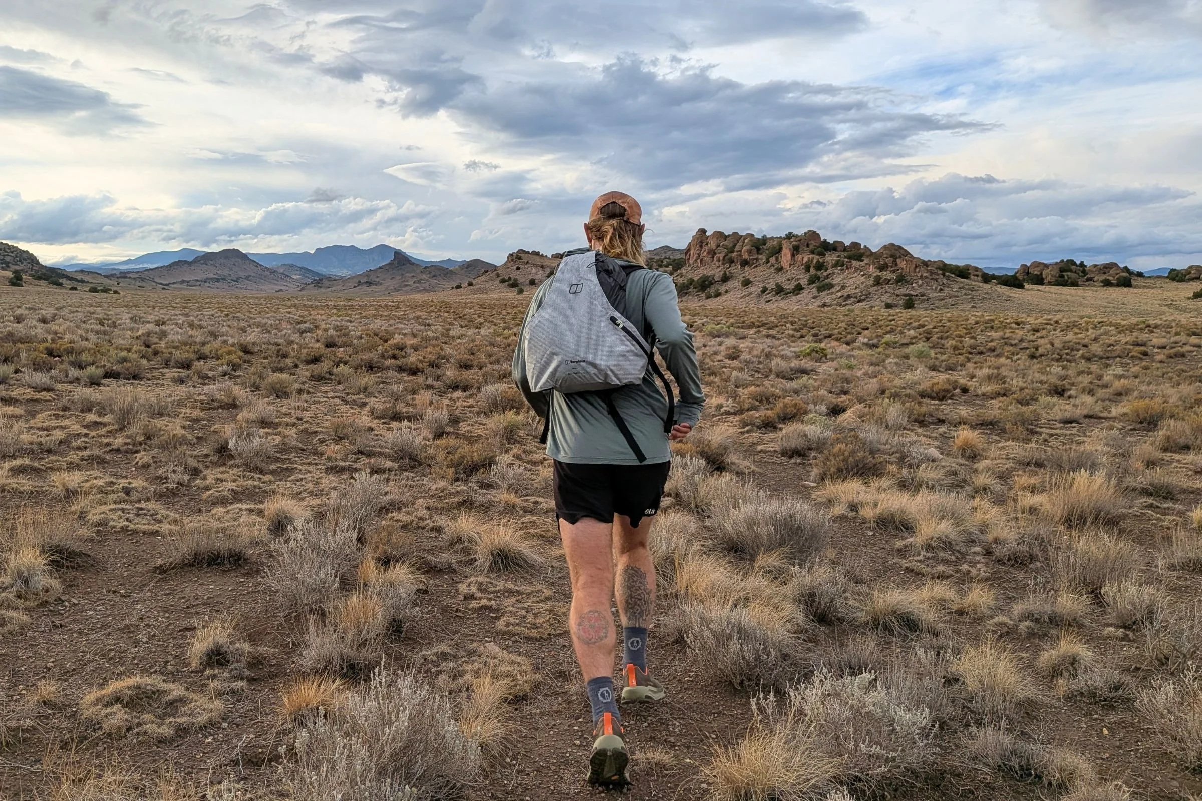A person wearing the Altra Olympus 7 and carrying a backpack walks through a field.