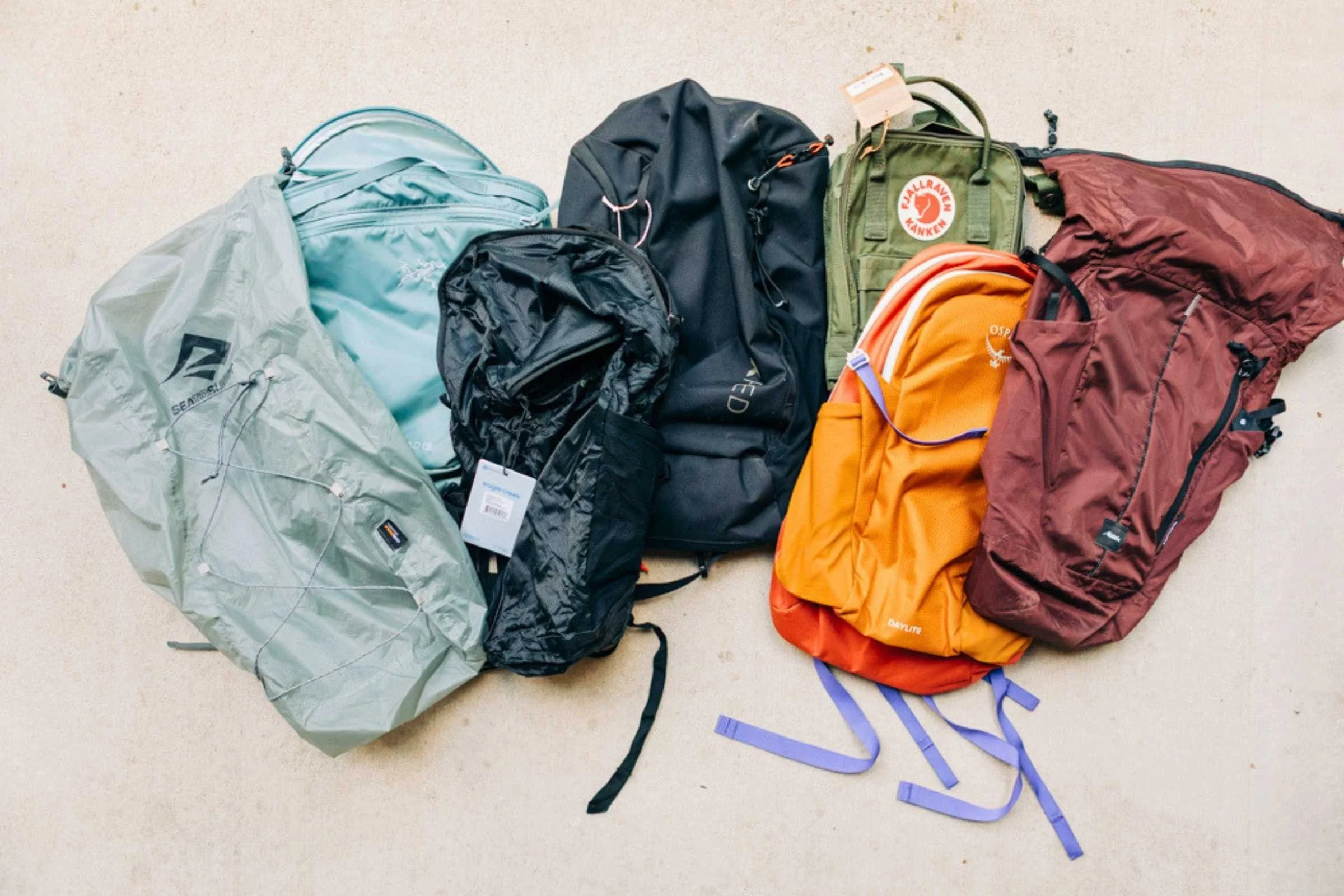 A selection of packable backpacks in various sizes arranged on a neutral surface, some stuffed into their own pockets