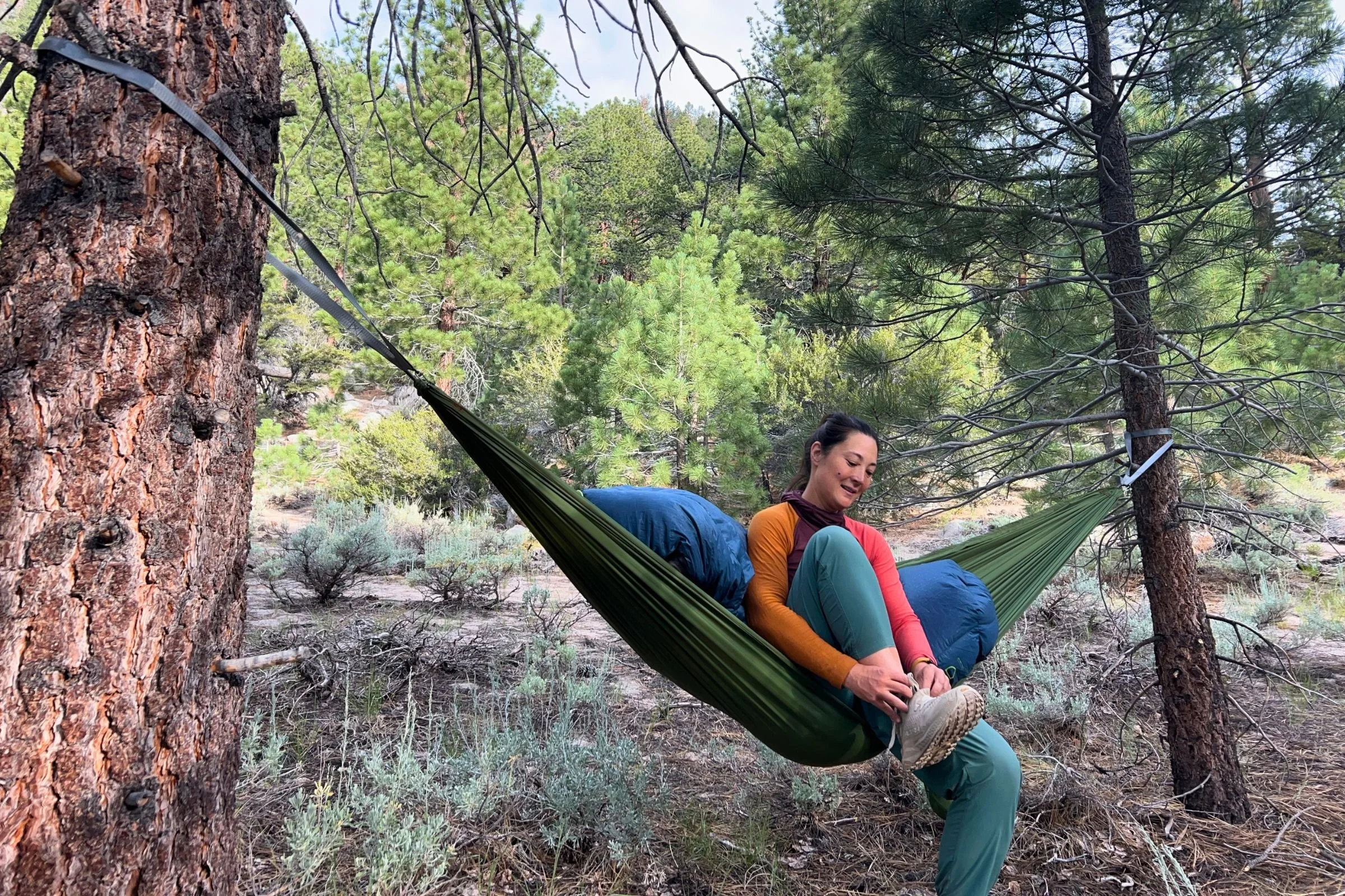 A woman rests in a hammock on top of an Exped Terra sleeping bag. Trees are in the background.