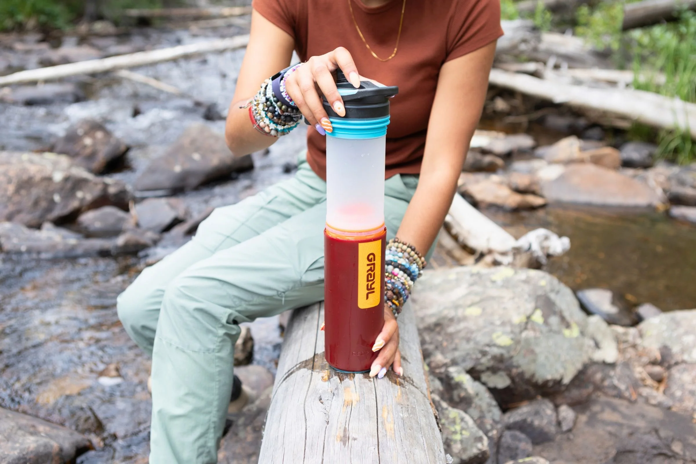 A woman holding a Grayl GeoPress Purifier while sitting on a log.