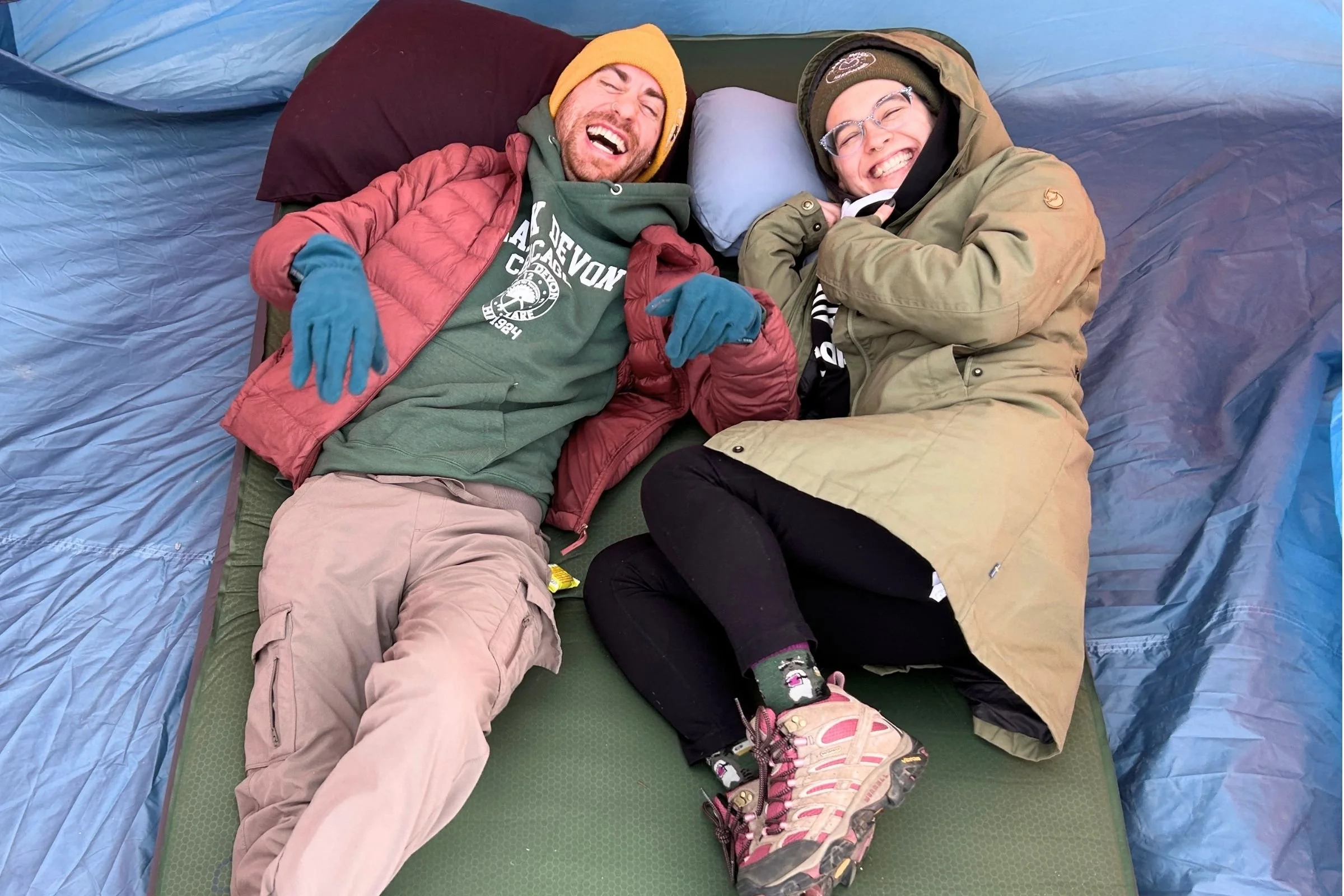 Two campers relax side by side on the EXPED LuxeMat inside a tent, showing the mattress’s spacious sleeping surface and plush comfort for car camping