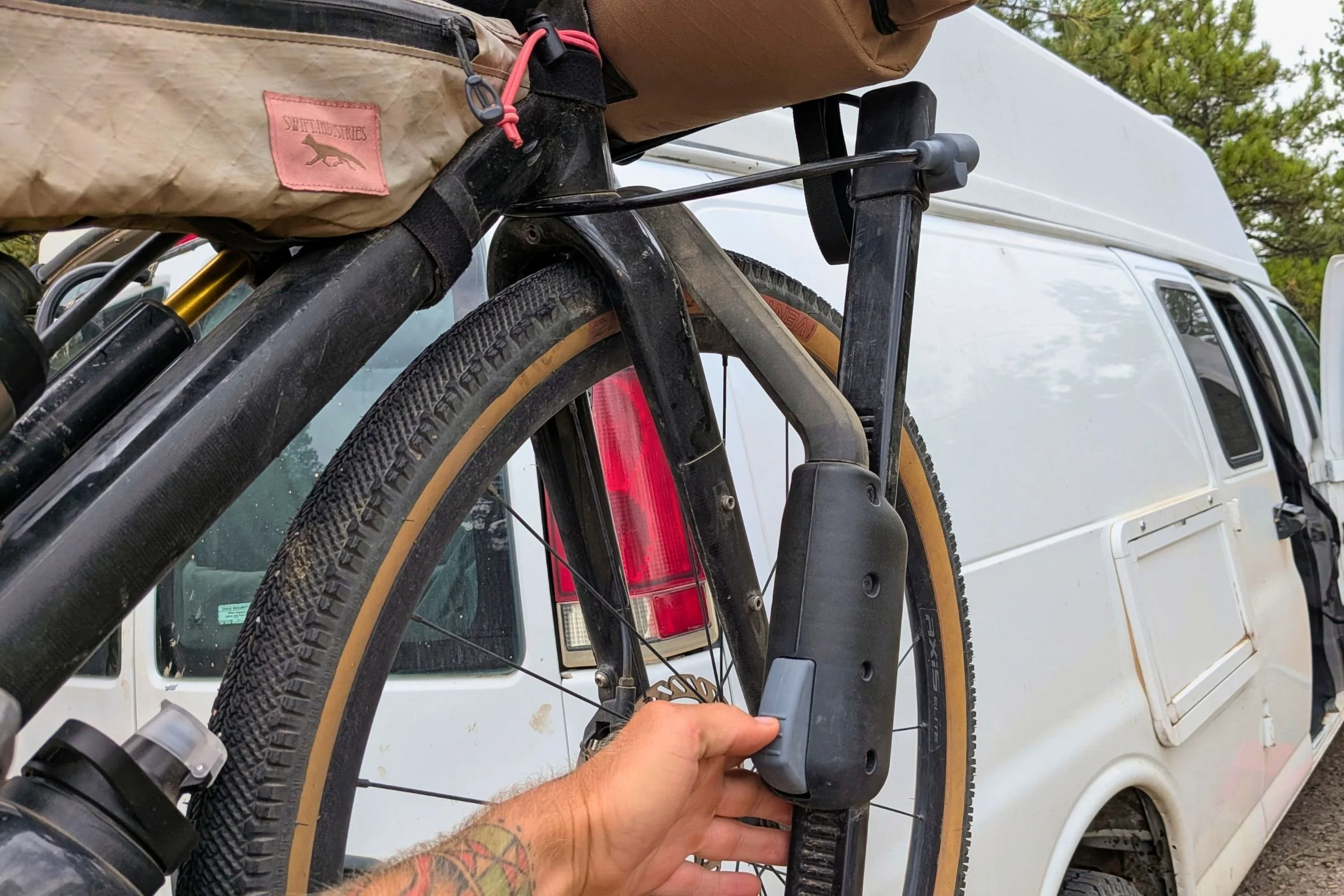 A man holds a bike with a backpack mounted on a Yakima EXO DoubleUp 2-Bike Hitch Rack.