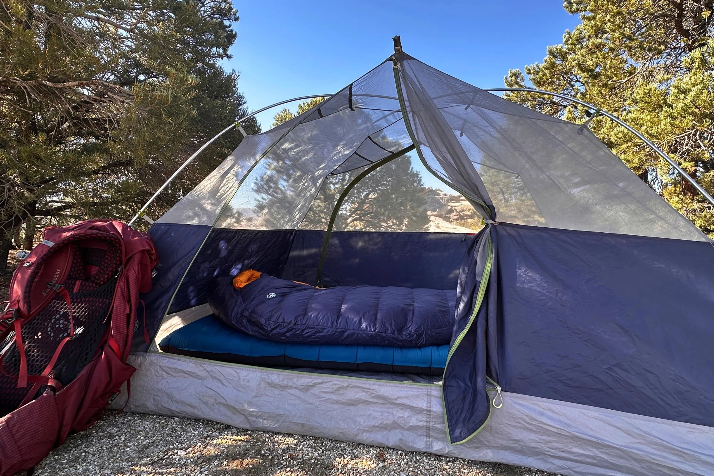 REI Co-op Magma 30 sleeping bag resting on a blue sleeping pad inside an open tent, with a red backpack beside the entrance