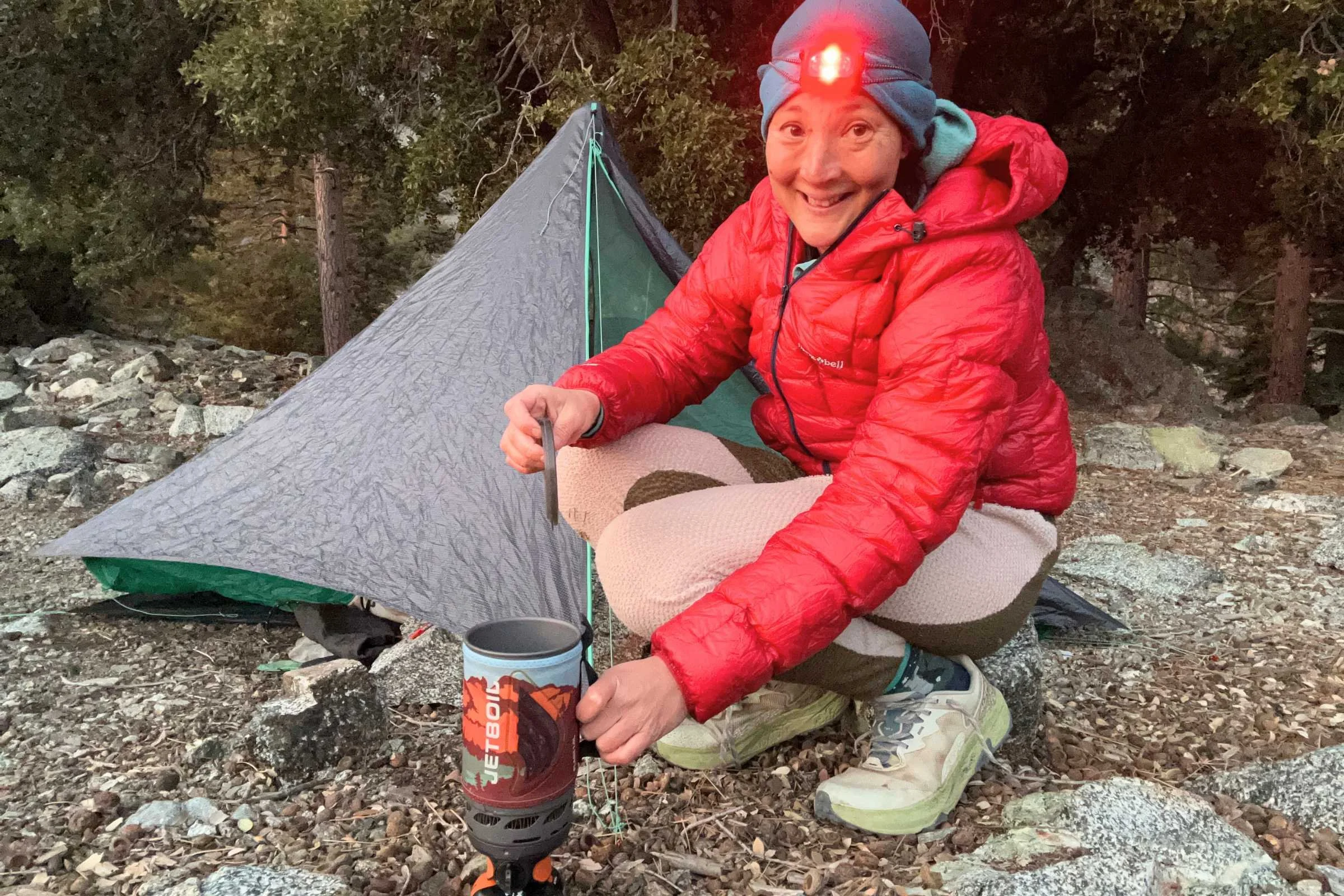 Camper wearing Nitecore NU25 MCT headlamp in red light mode while cooking on a Jetboil backpacking stove