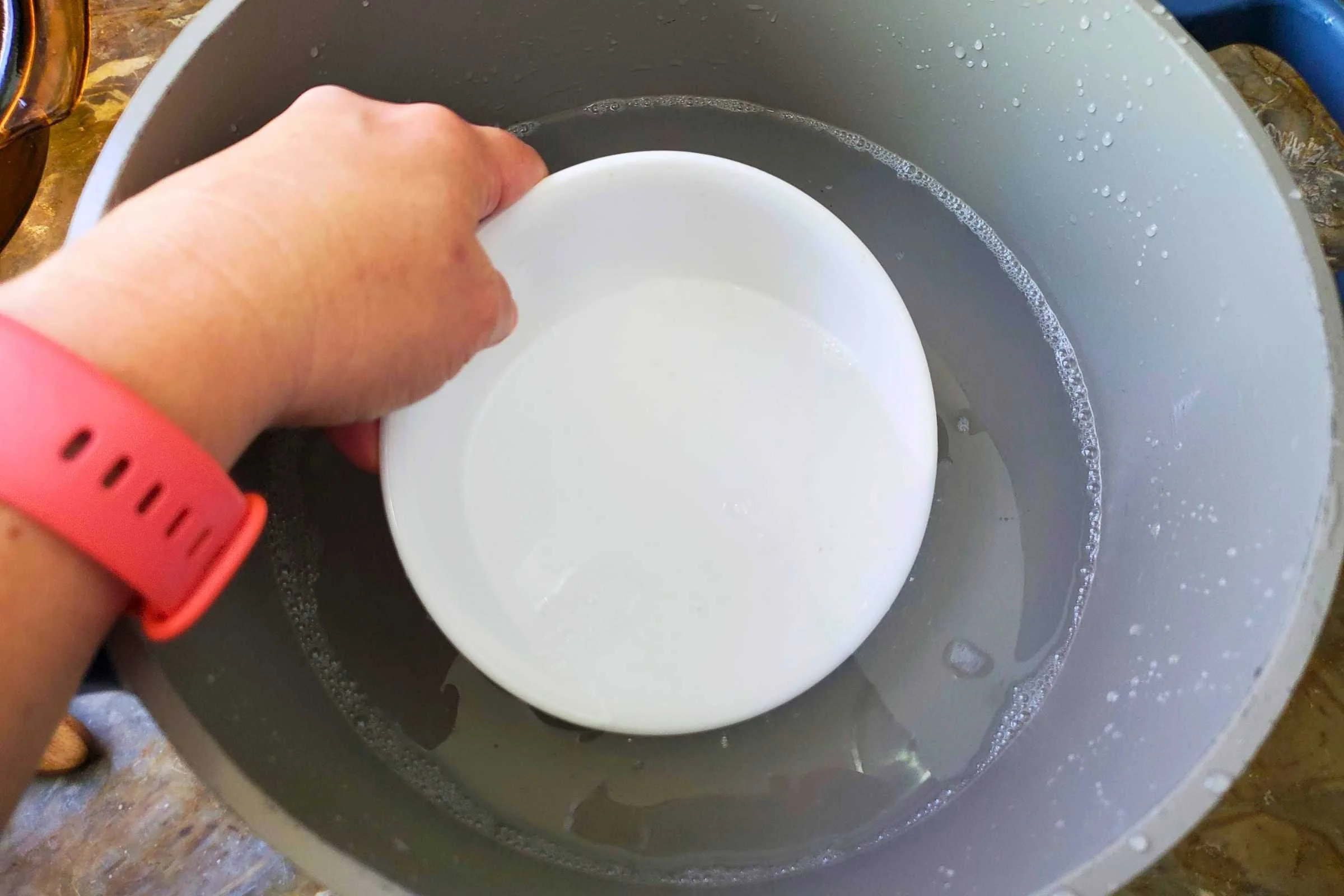A bowl is being rinsed in a pot of clear water.
