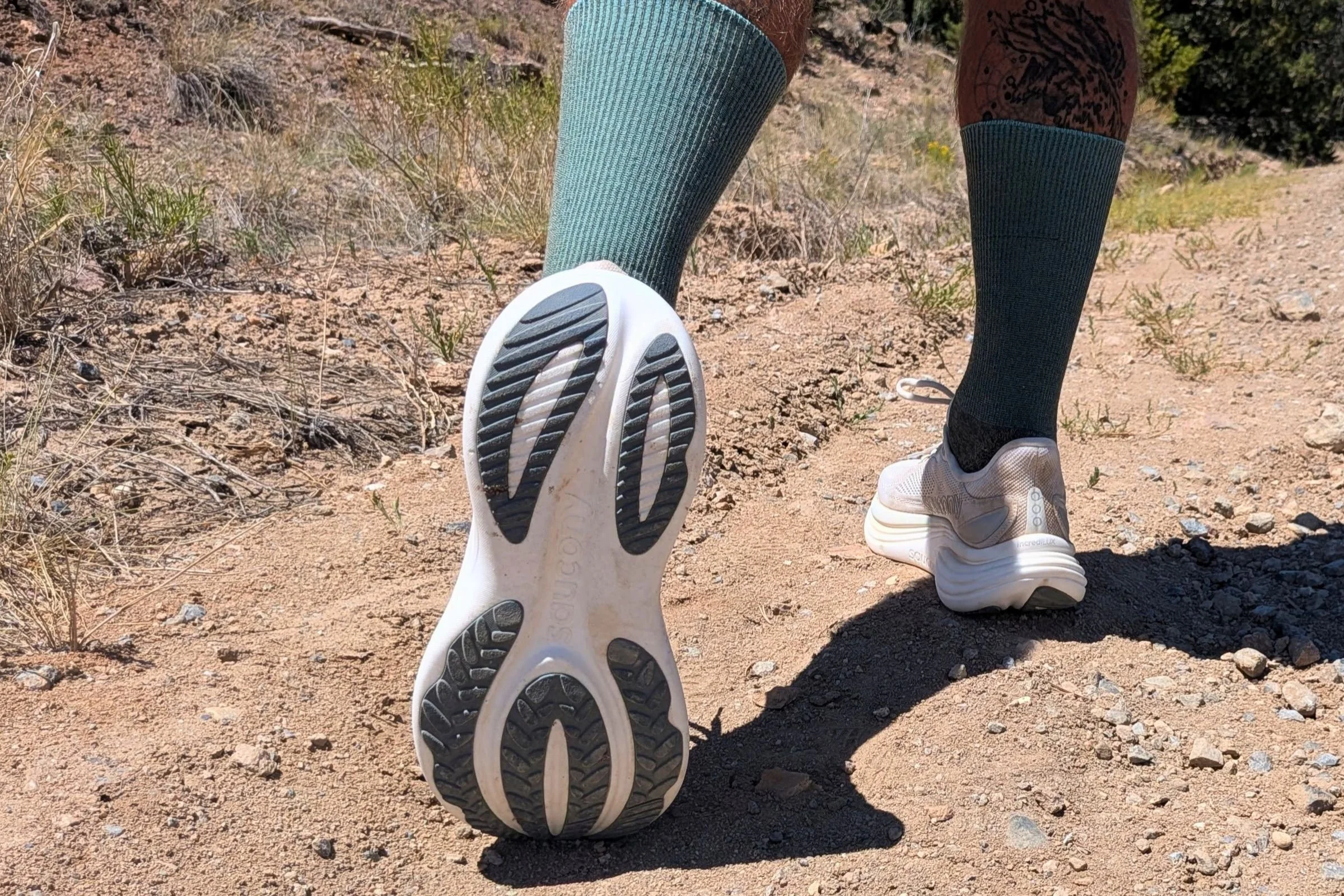 Close-up of a person wearing green socks and the Saucony Triumph 24 Road Running Shoe on a dirt road.