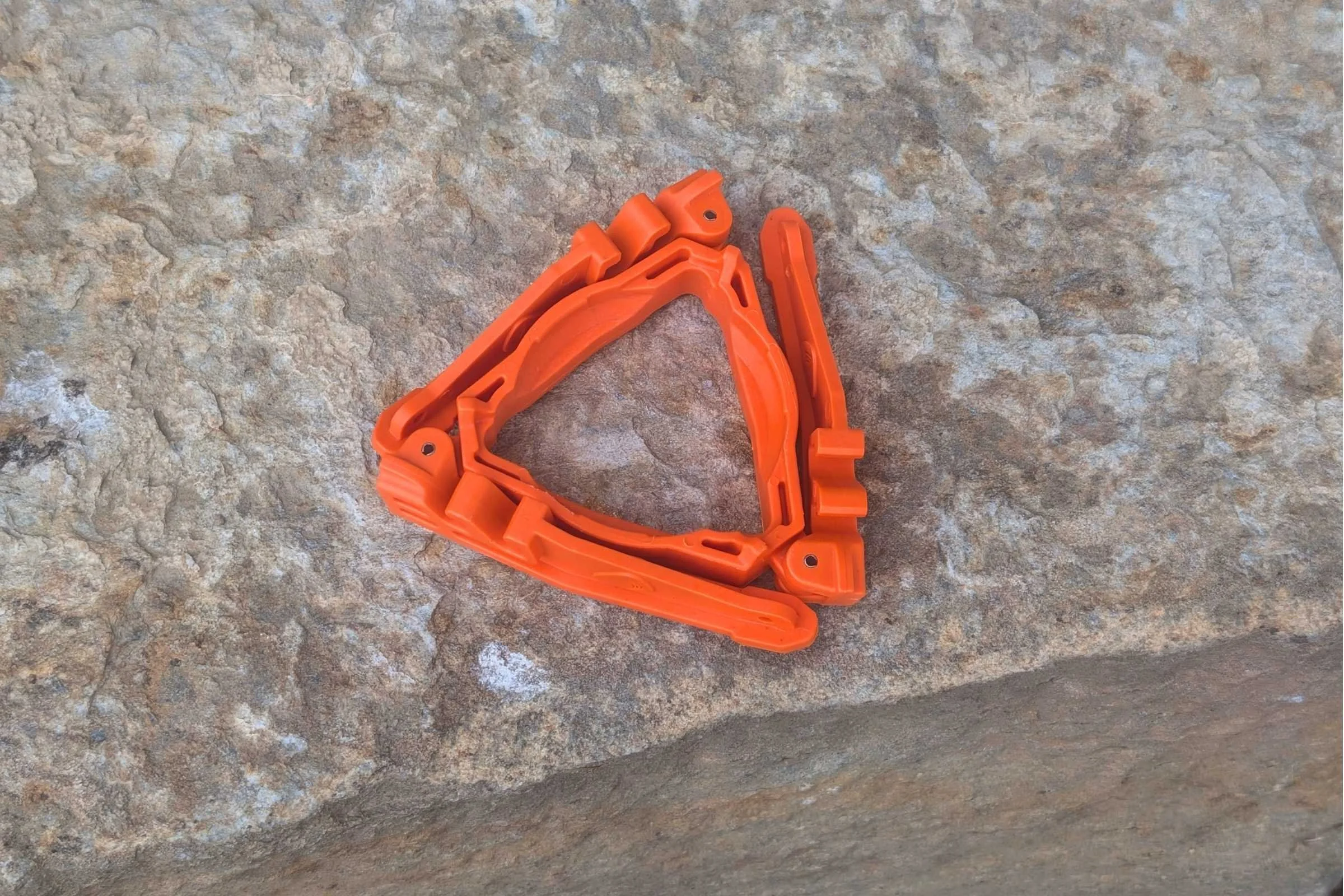 A closeup of the Jetboil TrailCook base folded up, orange color, on top of a rock.
