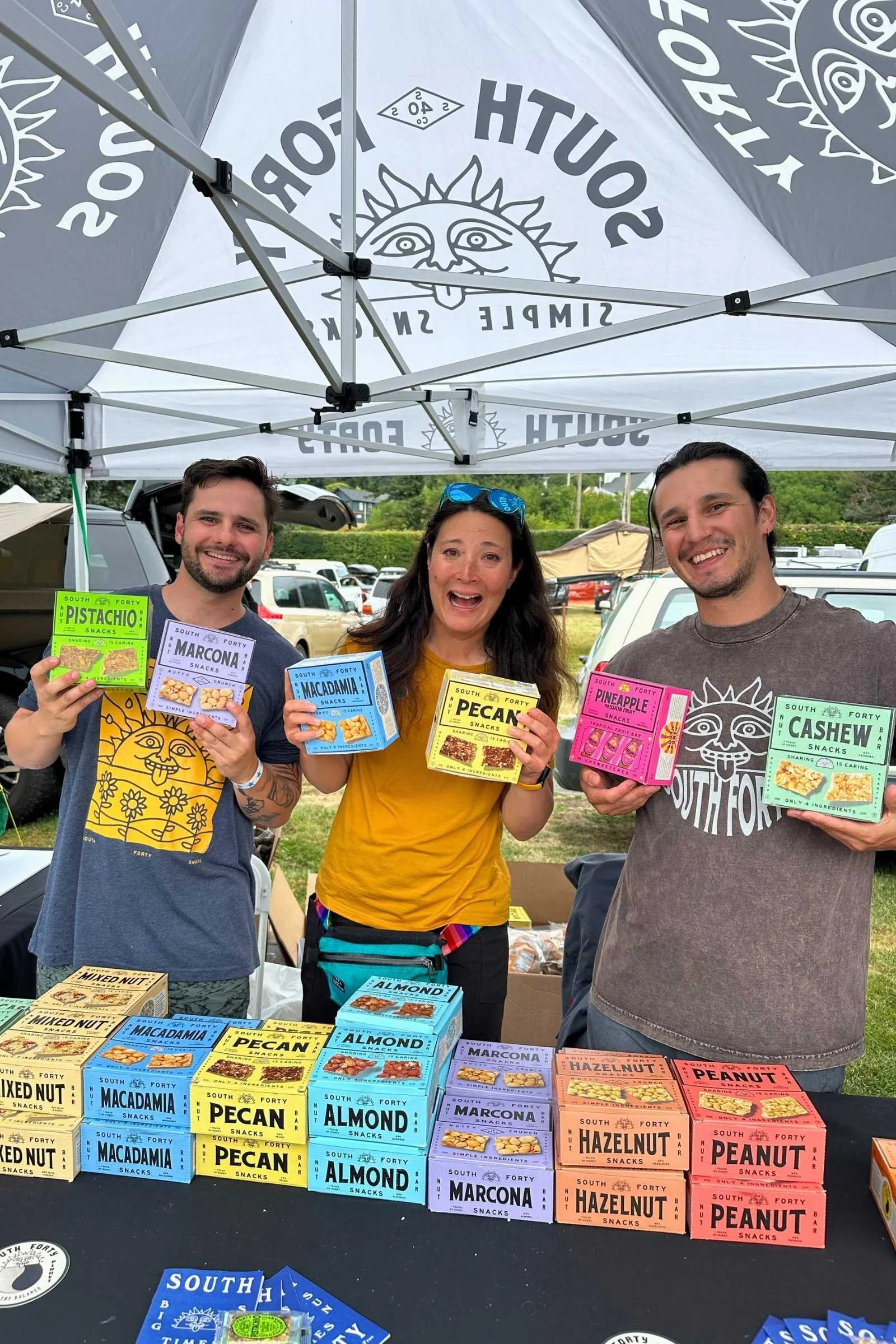 Liz Thomas standing between two other people, all three holding boxes of South Forty bars and standing behind several boxes of South Forty bars.