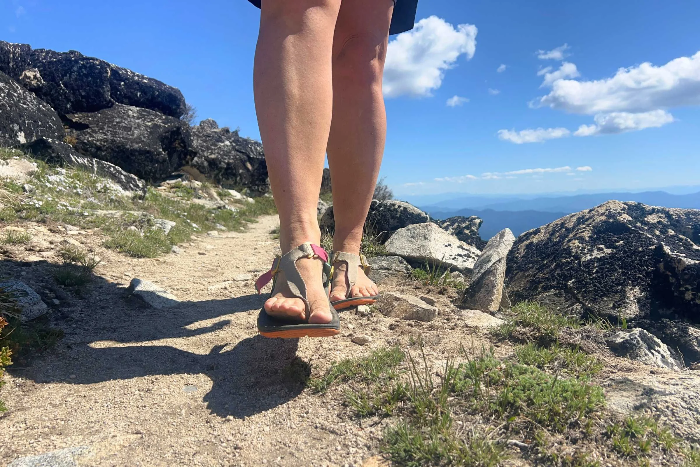 Person walking on a trail towards the camera with a close-up of their Lems Switchback Sandal Knit, so you can see the front strap style.