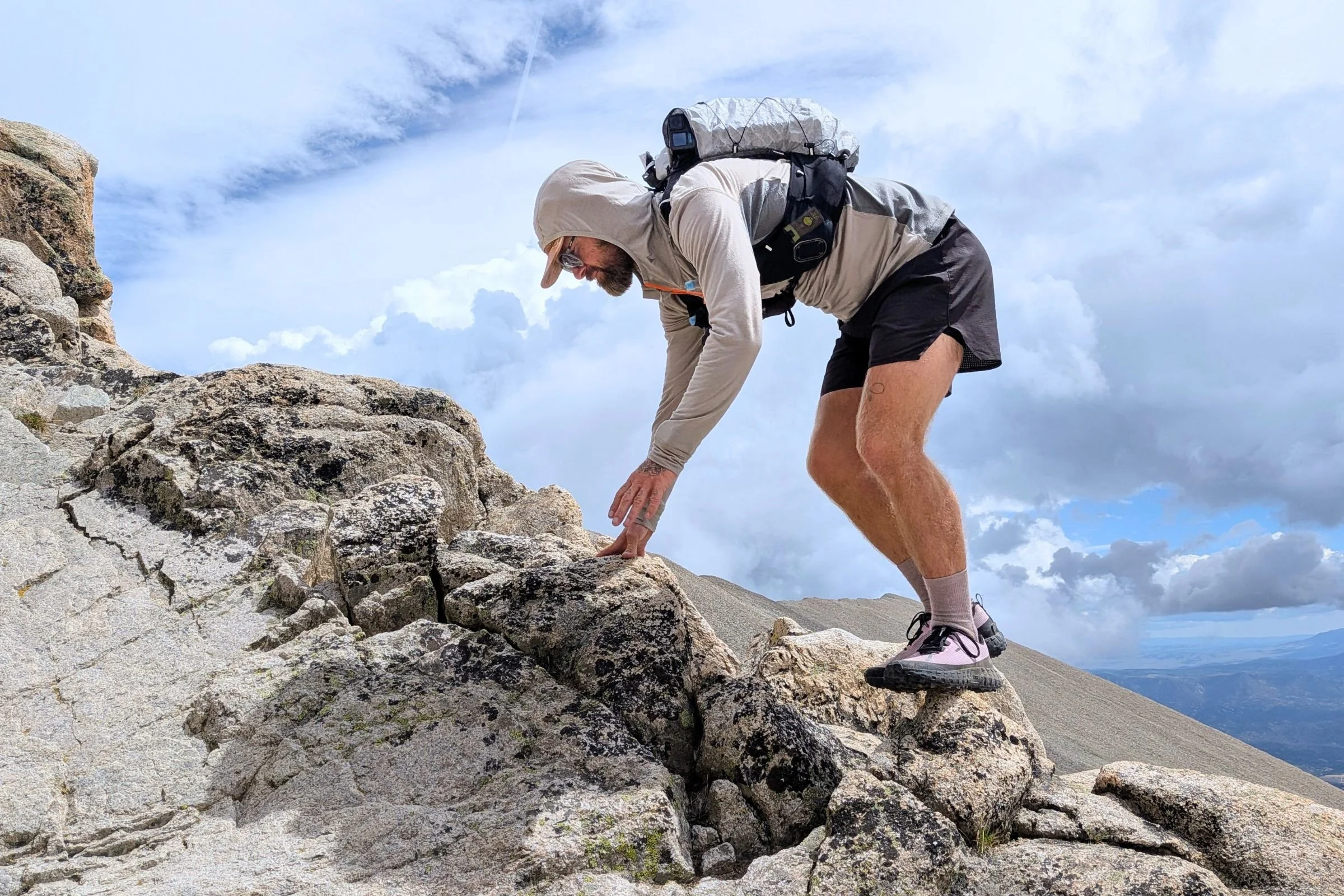 Man climbing a mountain with a backpack, wearing Norda 000 Trail Running Shoes.