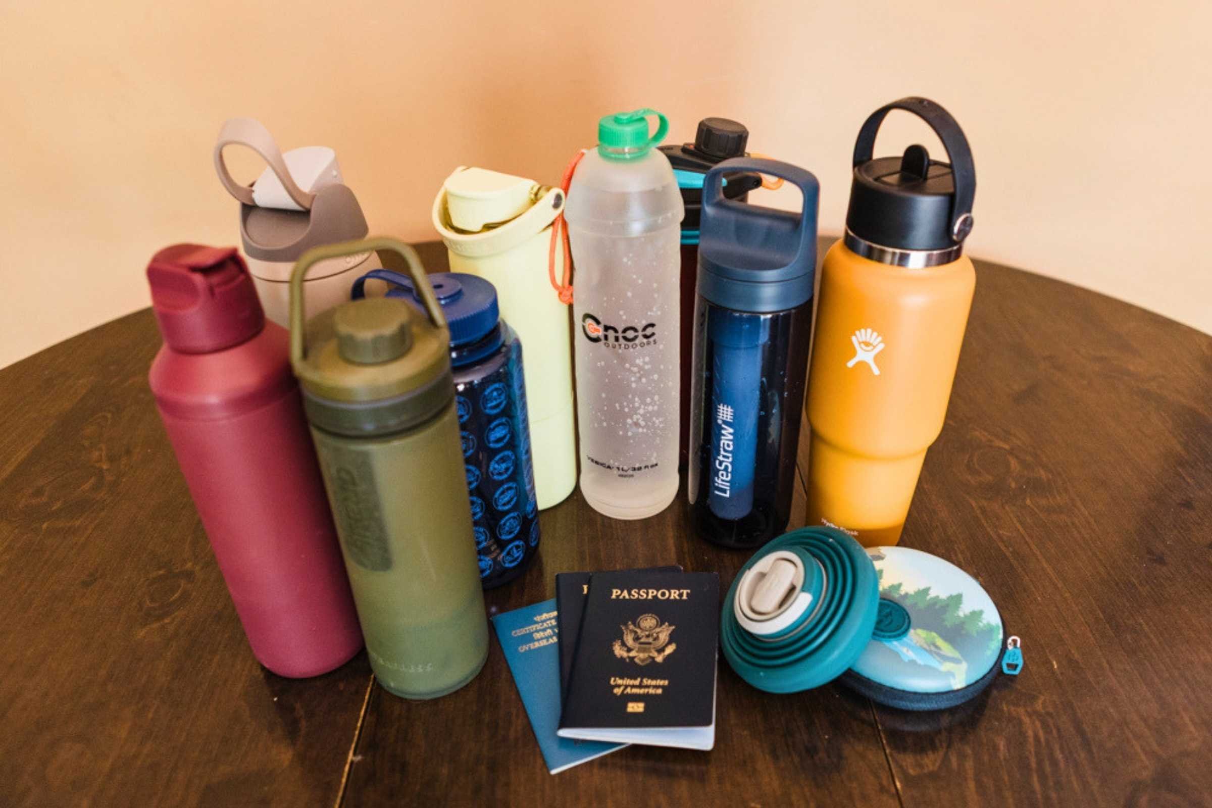 Assorted reusable drink bottles and travel mugs in different colors arranged on a wooden table