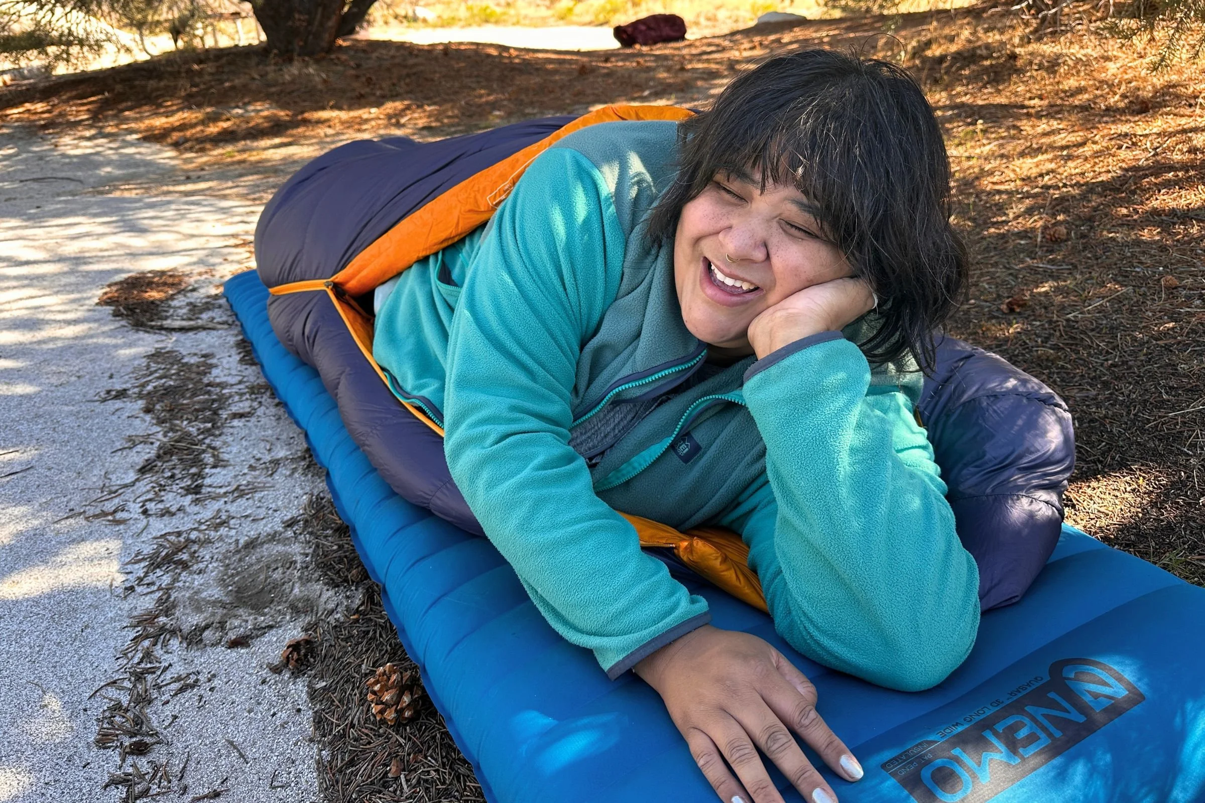 The tester after sleeping outside of the tent, smiling inside the REI Co-op Magma 30 sleeping bag.