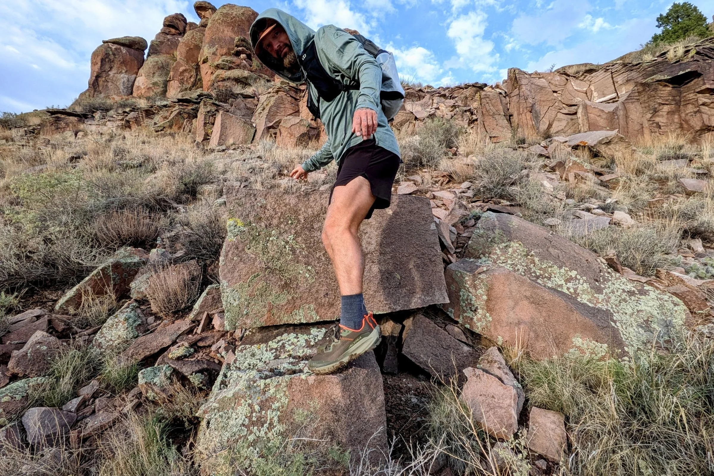 A man wearing the Altra Olympus 7 climbs over rocks in a desert landscape.