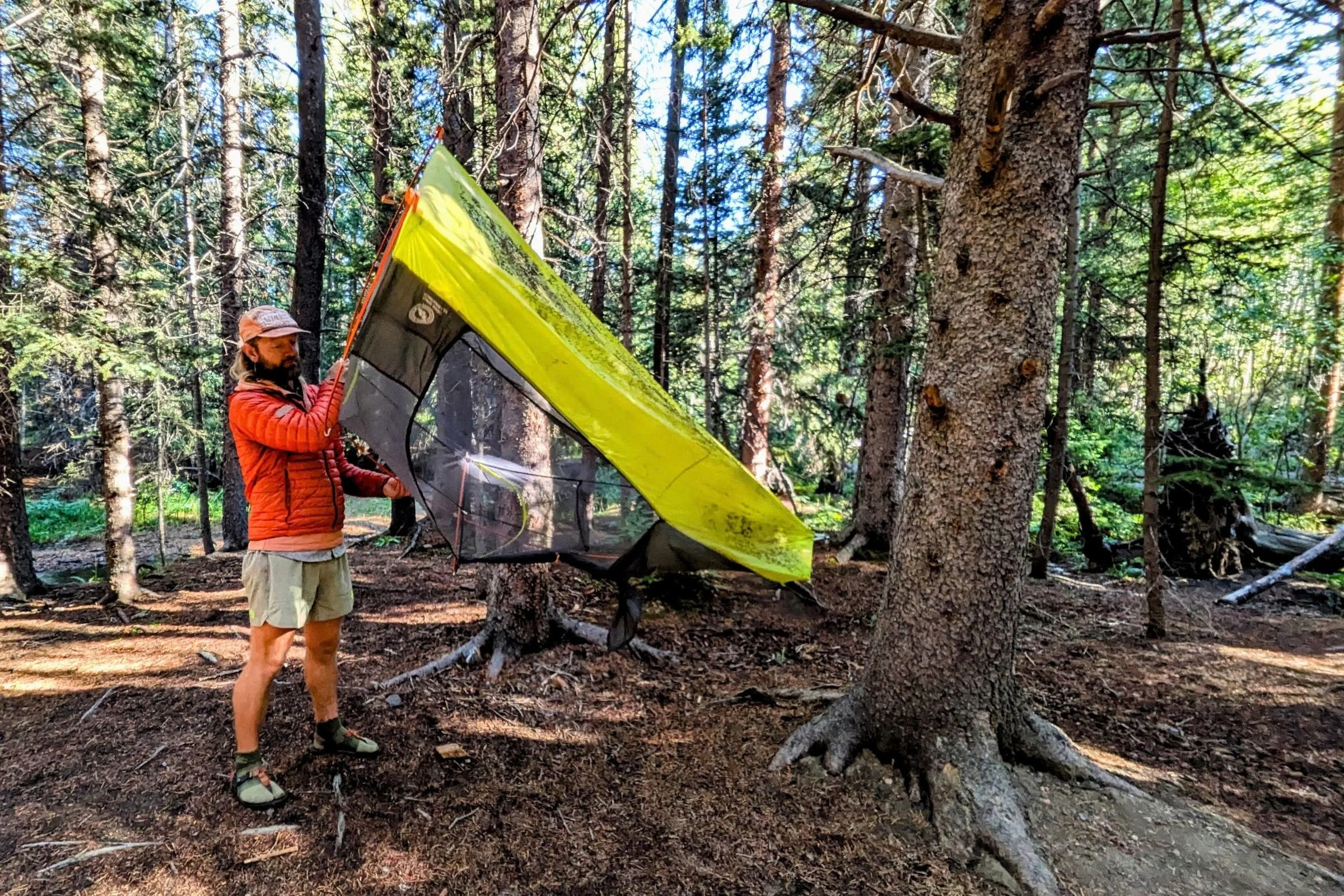 The author holding the Big Agnes Tiger Wall UL1 Bikepack Tent upside down to shake out dirt and debris with a forest in the background.