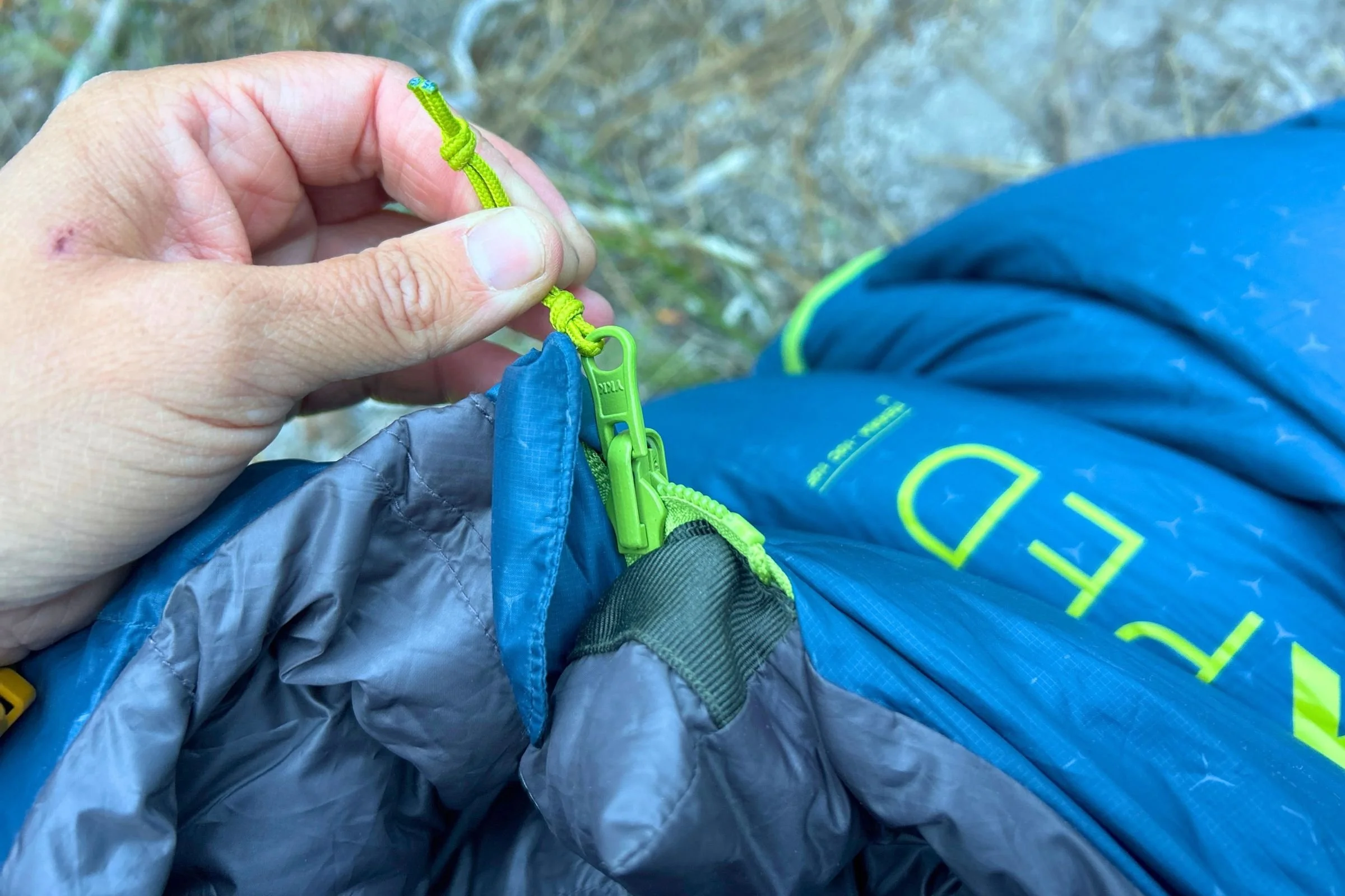 A person holds an Exped Terra Sleeping Bag open, showing its zipper.