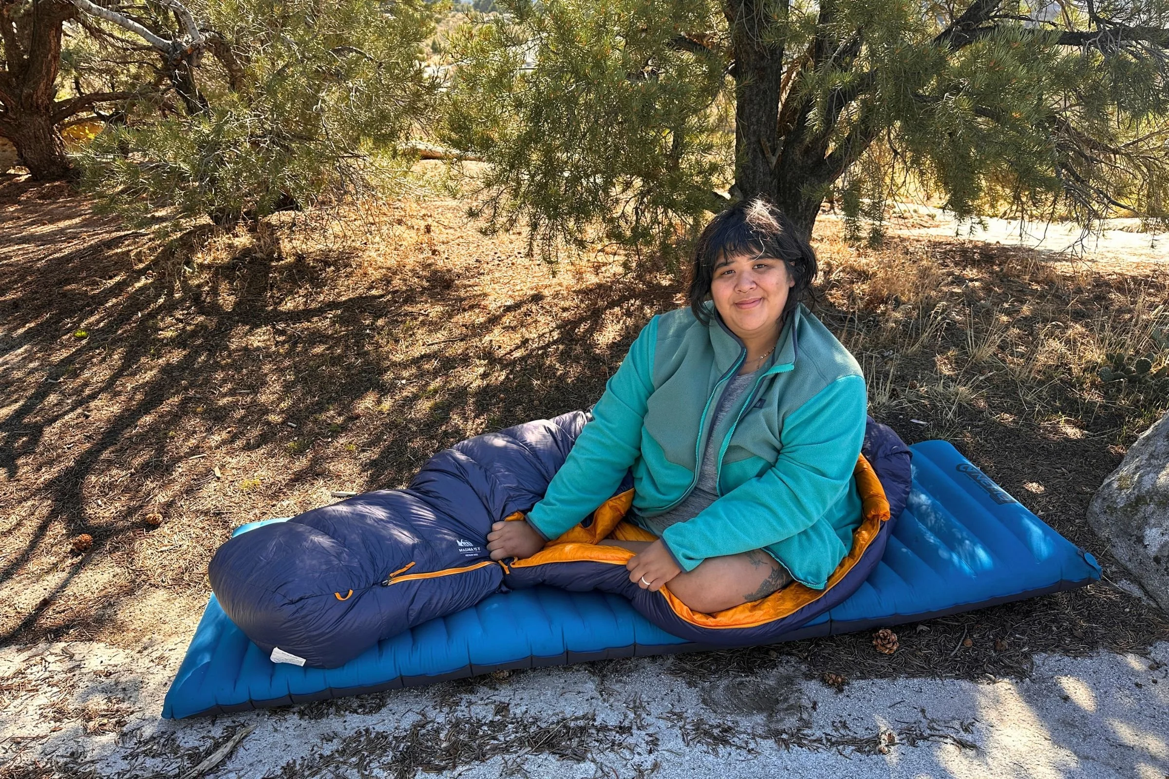 Tester sitting in the REI Co-op Magma 30 sleeping bag on a sleeping pad outdoors.