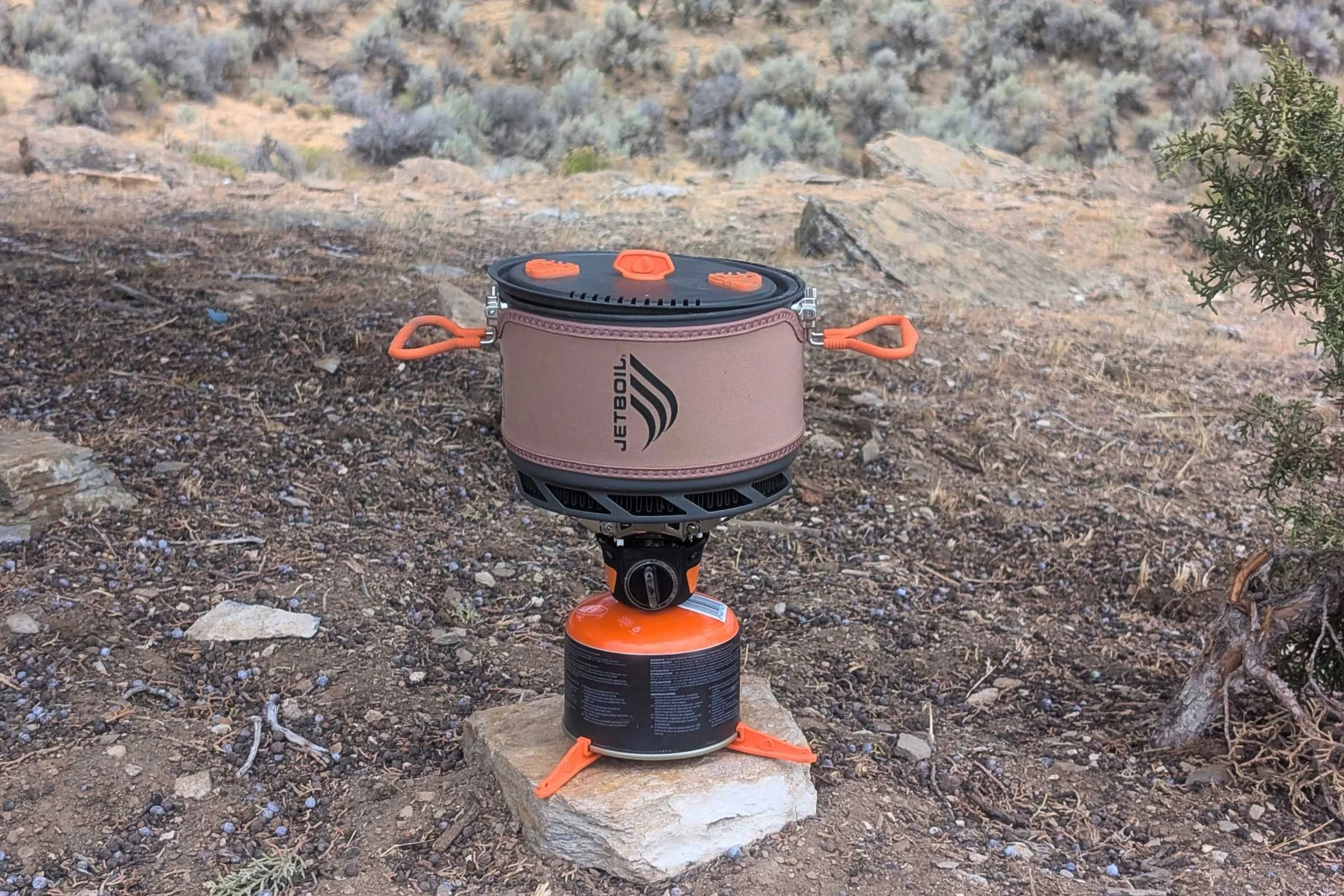 The Jetboil TrailCook set up on a rock with the pot on top and trees in the background.