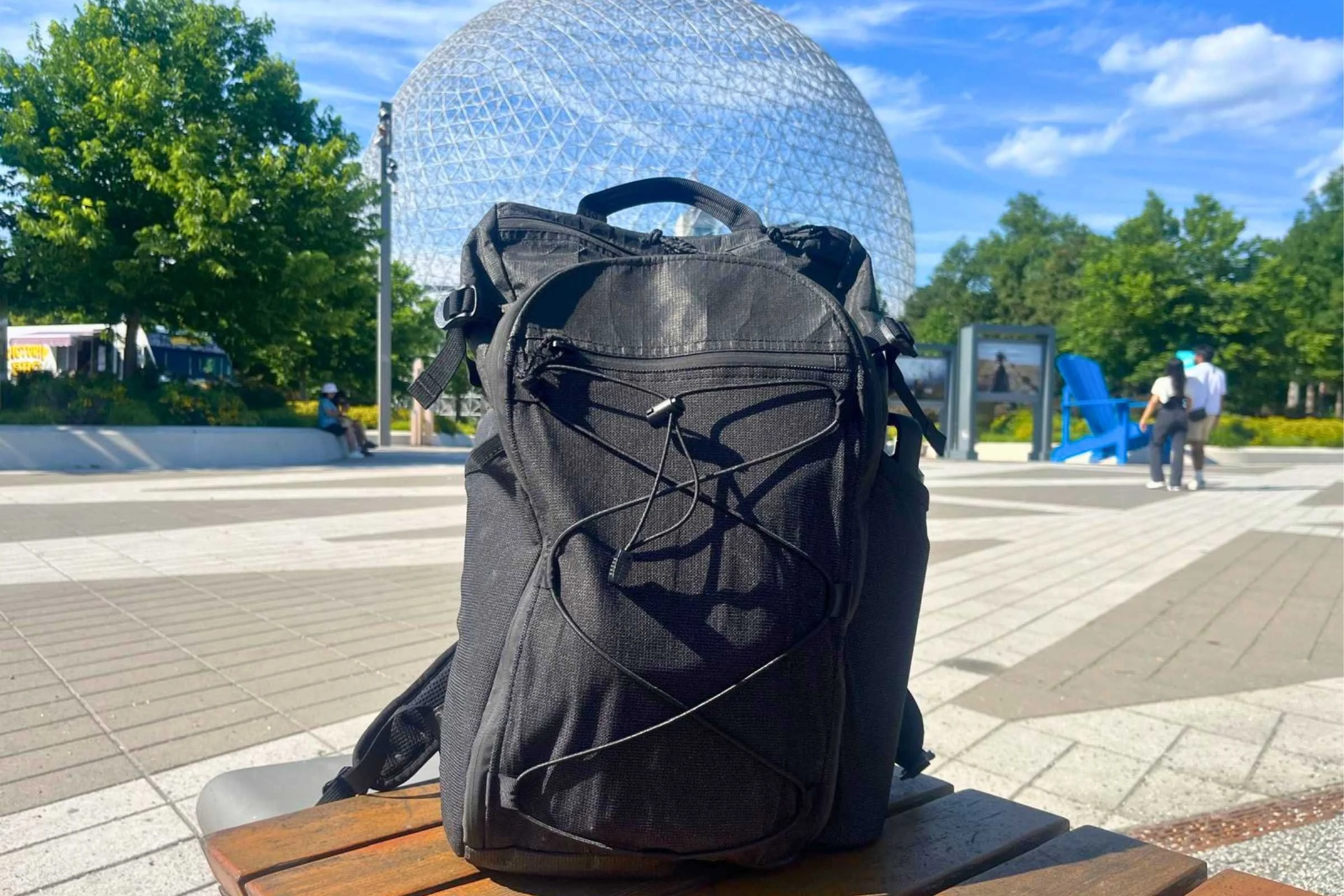 ULA Ultra Dragonfly 30L Adventure Travel Backpack on a wooden bench in front of a white geodesic dome.