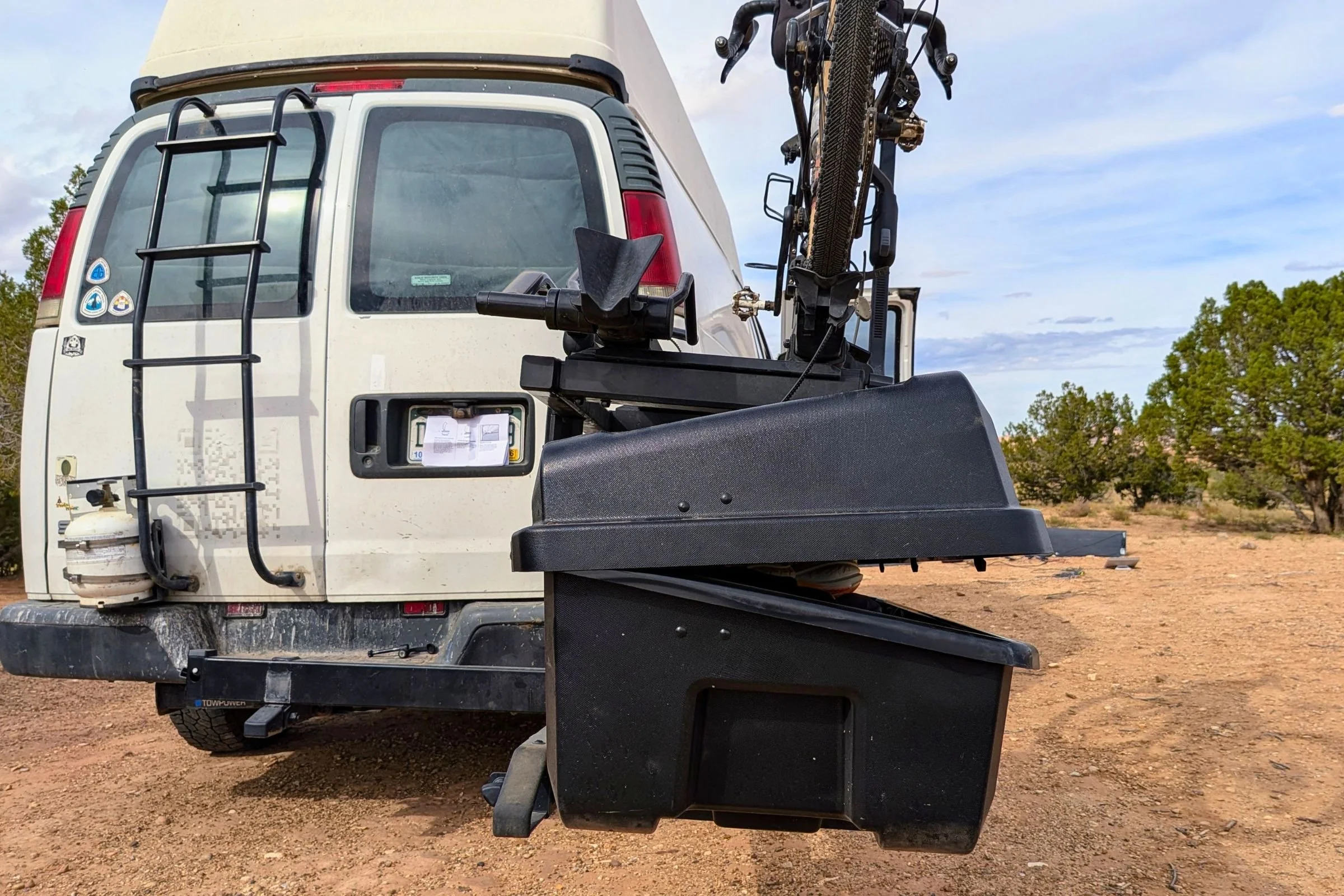 Yakima EXO GearLocker with its lid partly open beneath an EXO TopShelf and bike rack behind a van.