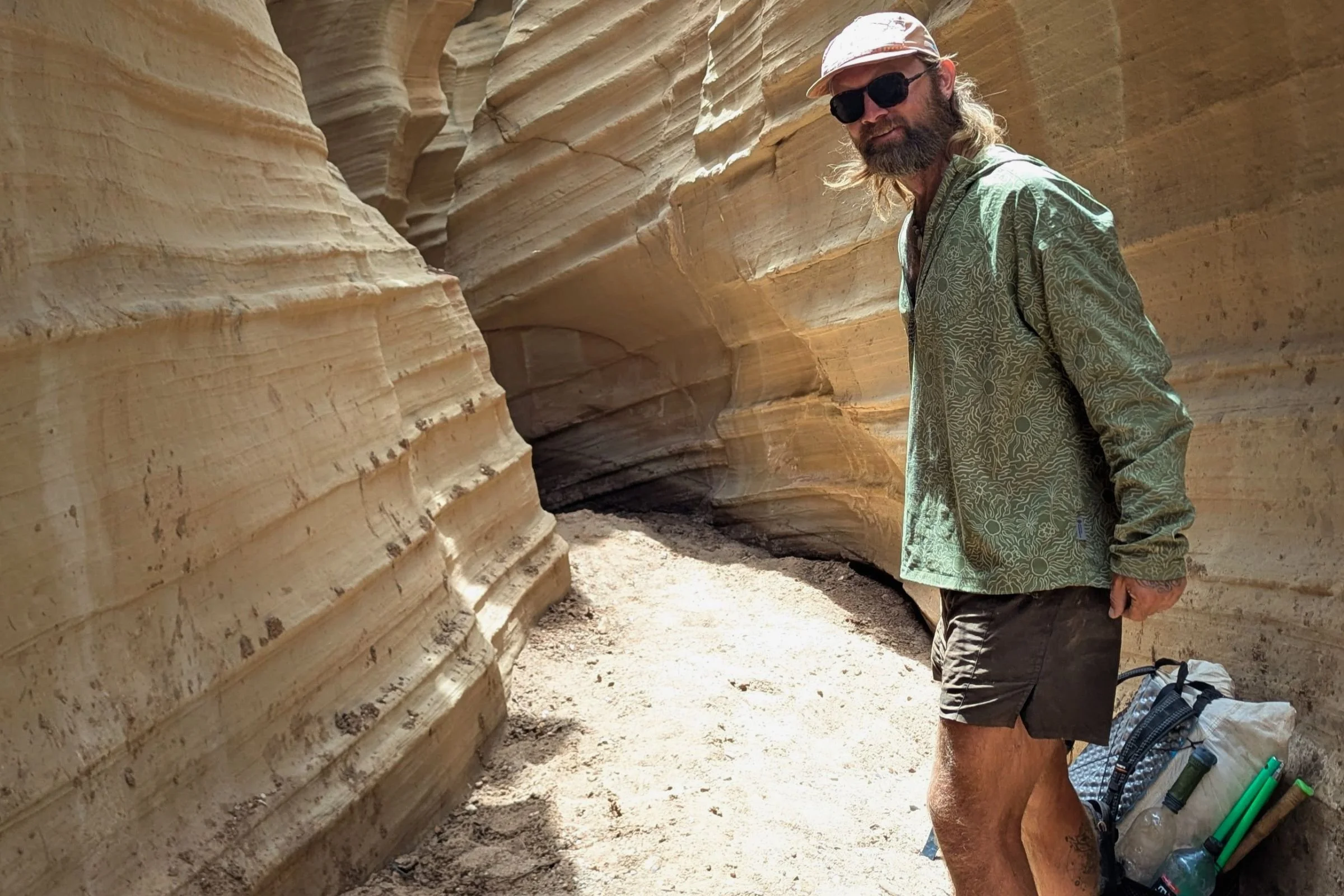 Man in Patagonia Strider Pro shorts, wearing sunglasses and a backpack, standing in a narrow canyon.