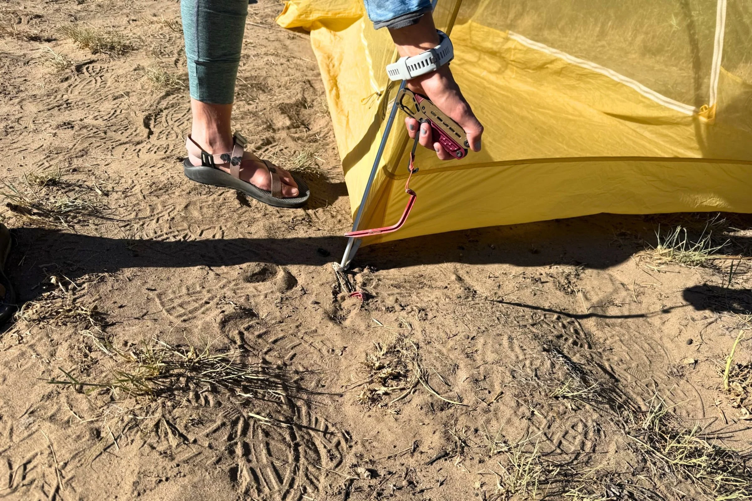 Mary uses the Gerber Stakeout Spark’s stake puller to remove a bent tent stake beside a yellow tent.