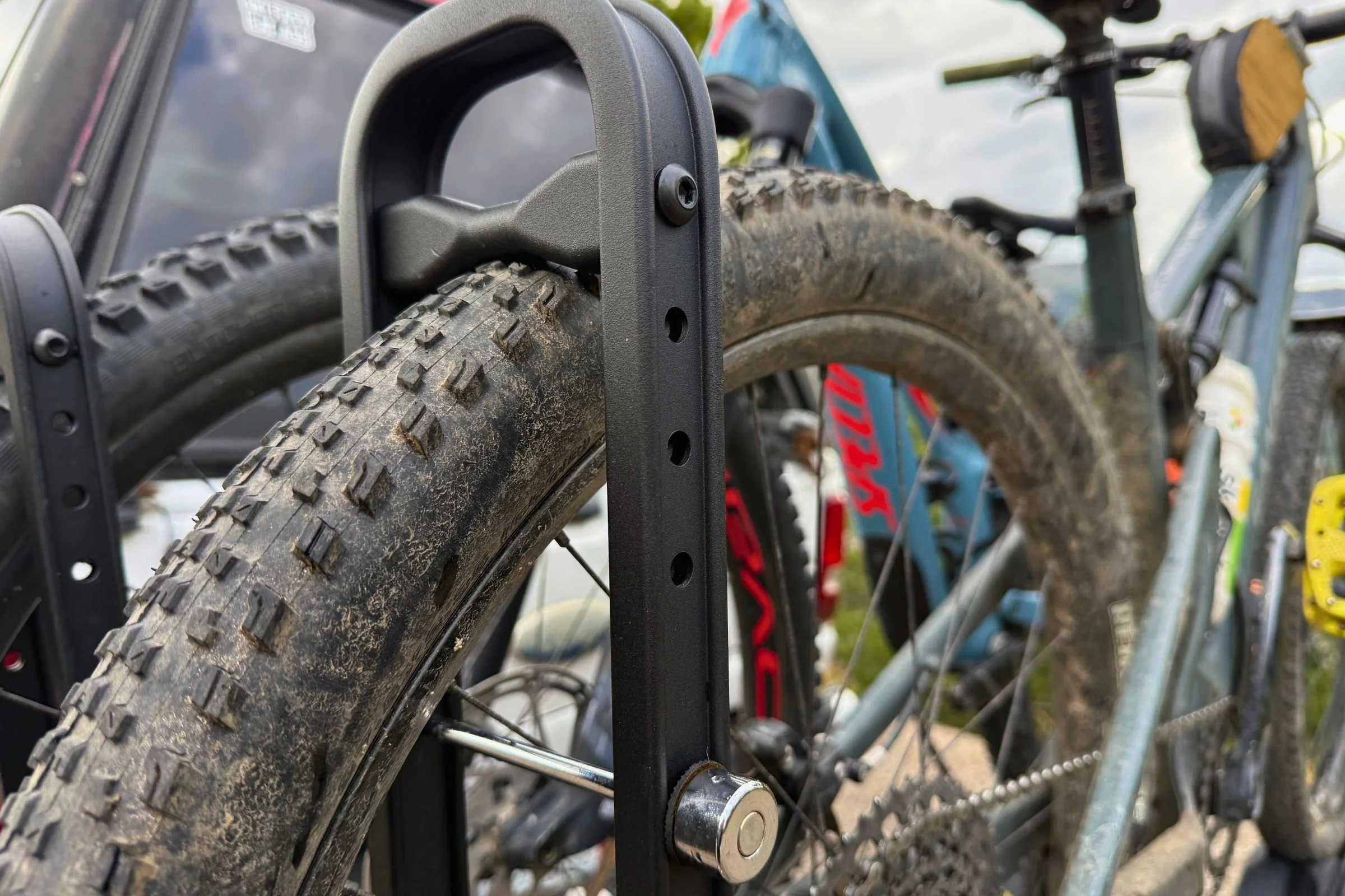 A bicycle parked beside a car equipped with a Hollywood Racks CrossTrack Hitch Bike Rack, showing the wheel-clamp detail.