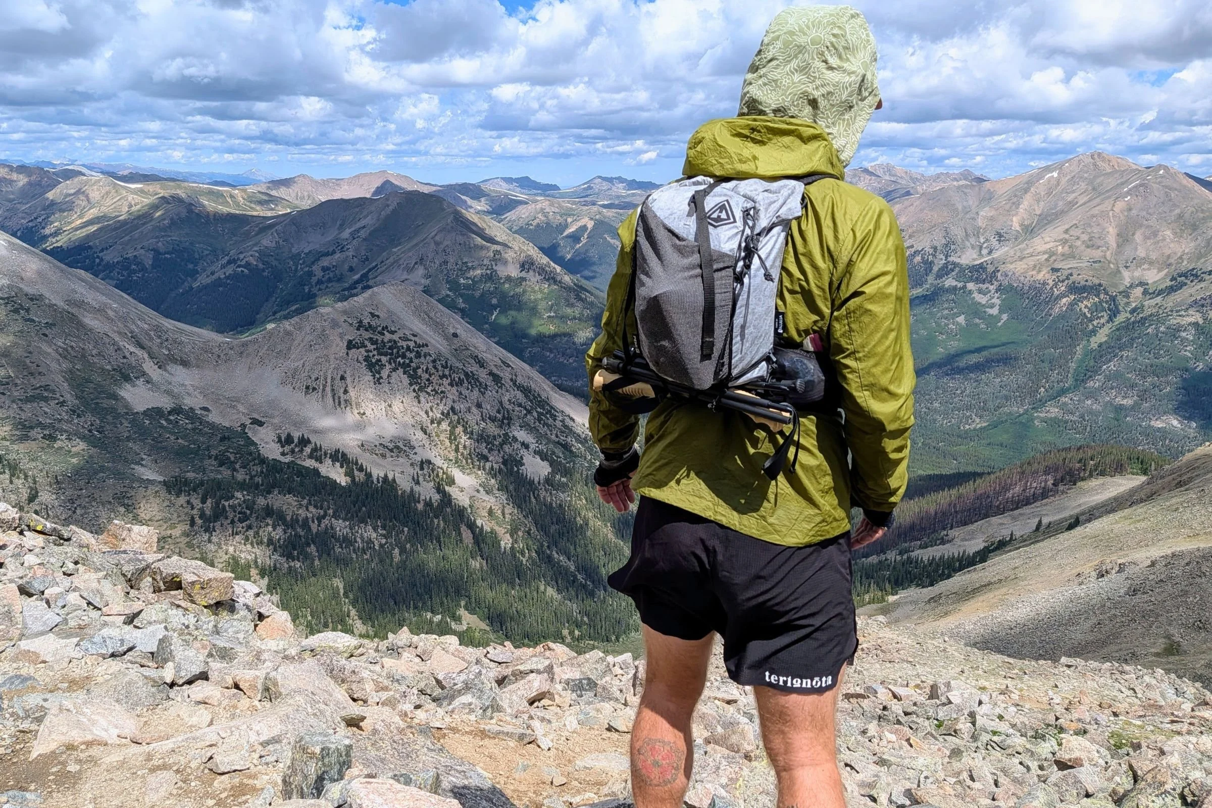 Man wearing a backpack and Terignota Sendero Shorts while standing on a mountain summit.