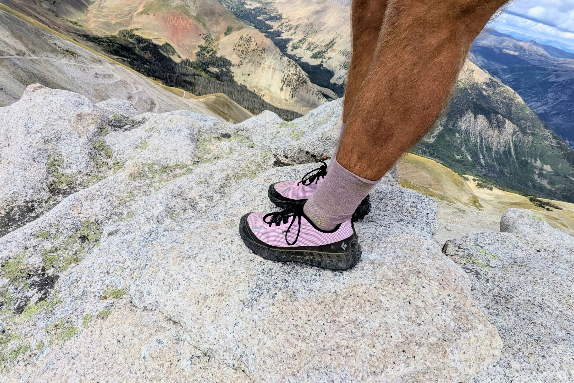 Man wearing pink Norda 000 Trail Running Shoes standing on a rock in the woods.