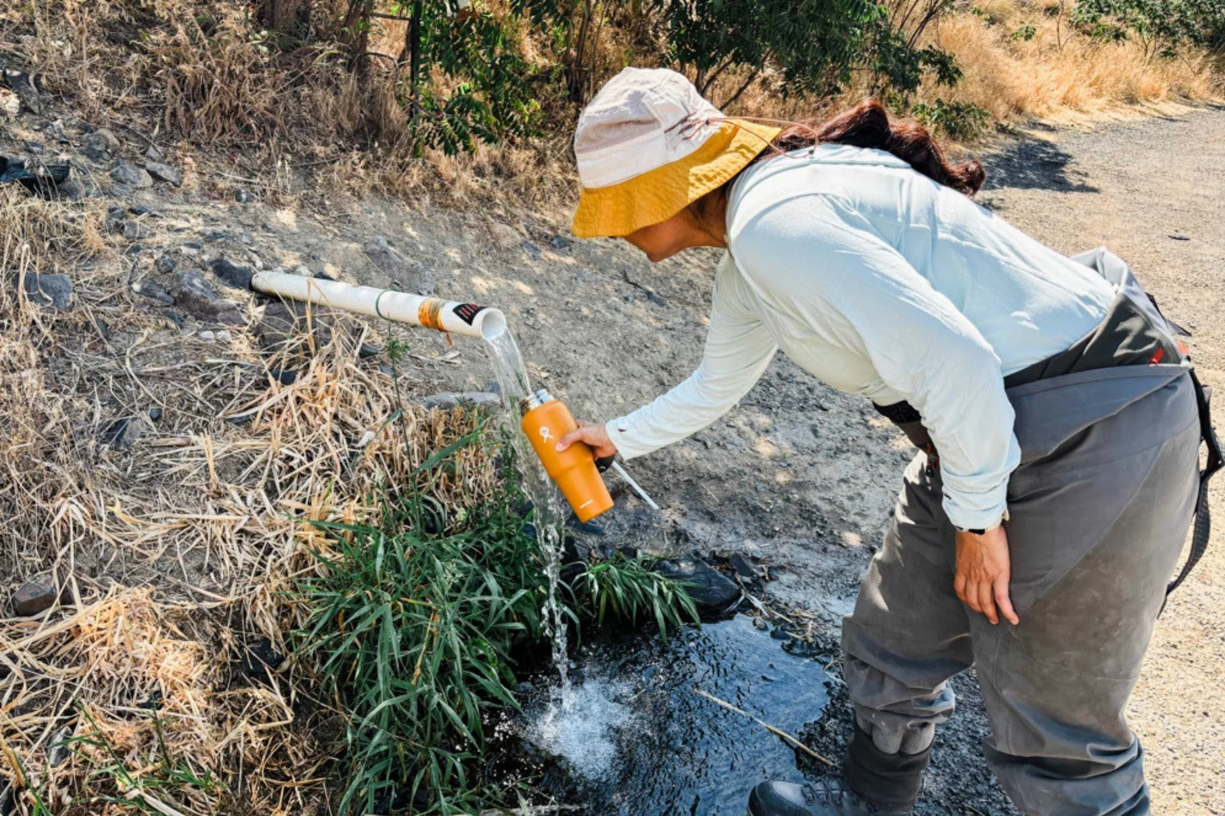 A person filling a Hydro Flask travel water bottle in a stream