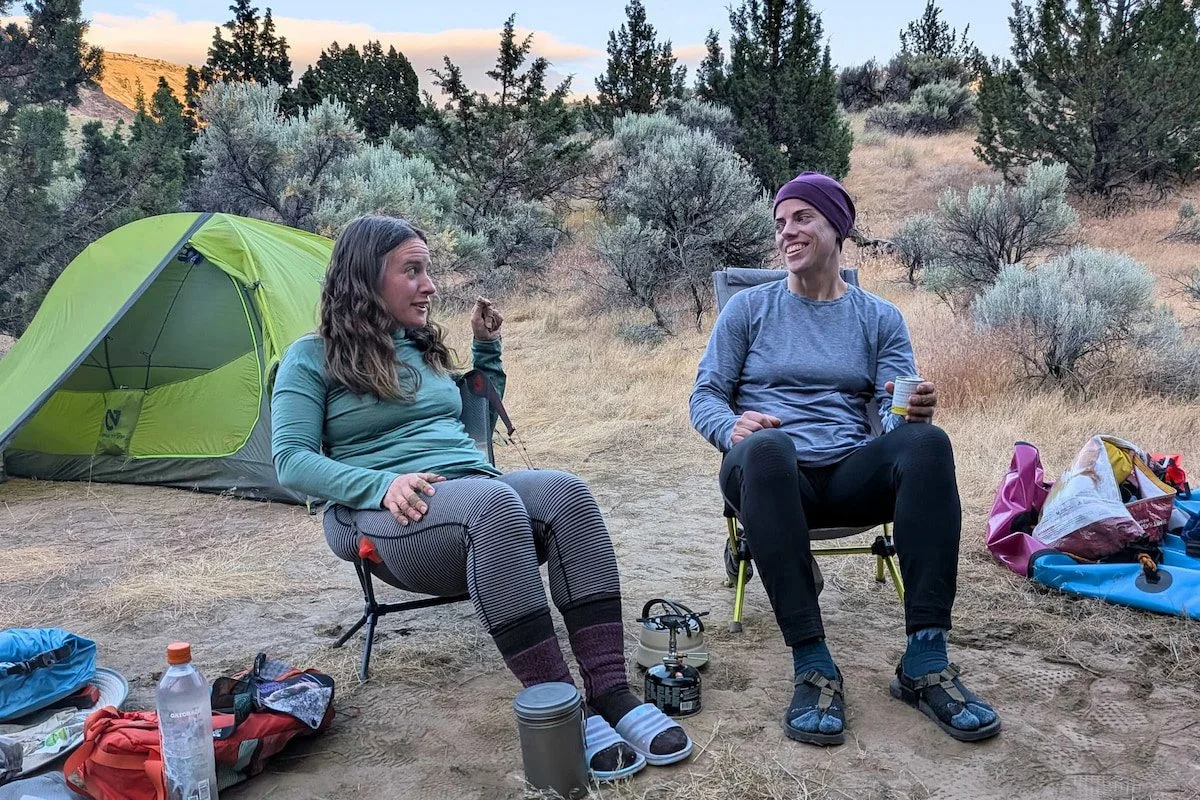 Two people sitting in camp chairs with a green tent in the background