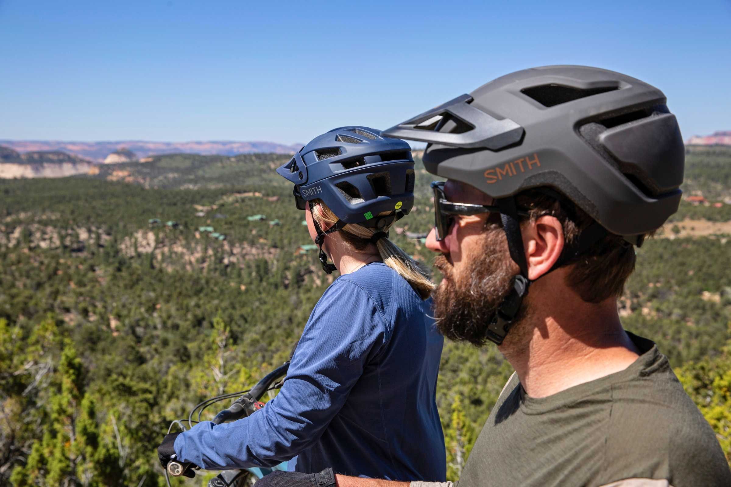 Woman wearing the Smith Engage helmet in dark blue next to a man wearing a Smith Pilot MTB helmet in dark grey.