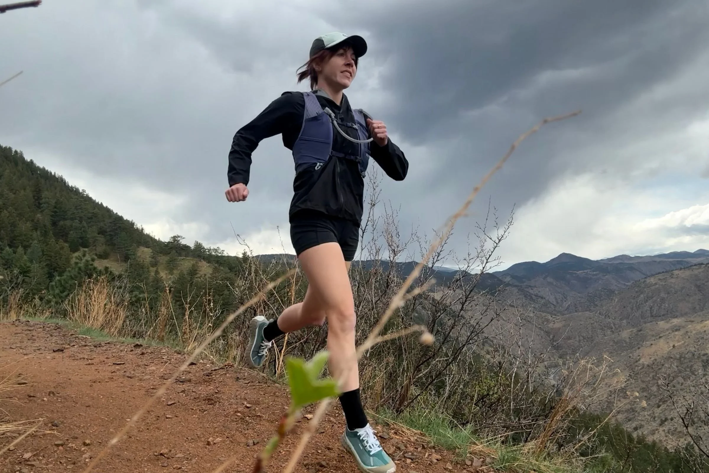 Woman trail running uphill through a mountainous landscape, wearing Nathan VaporAir