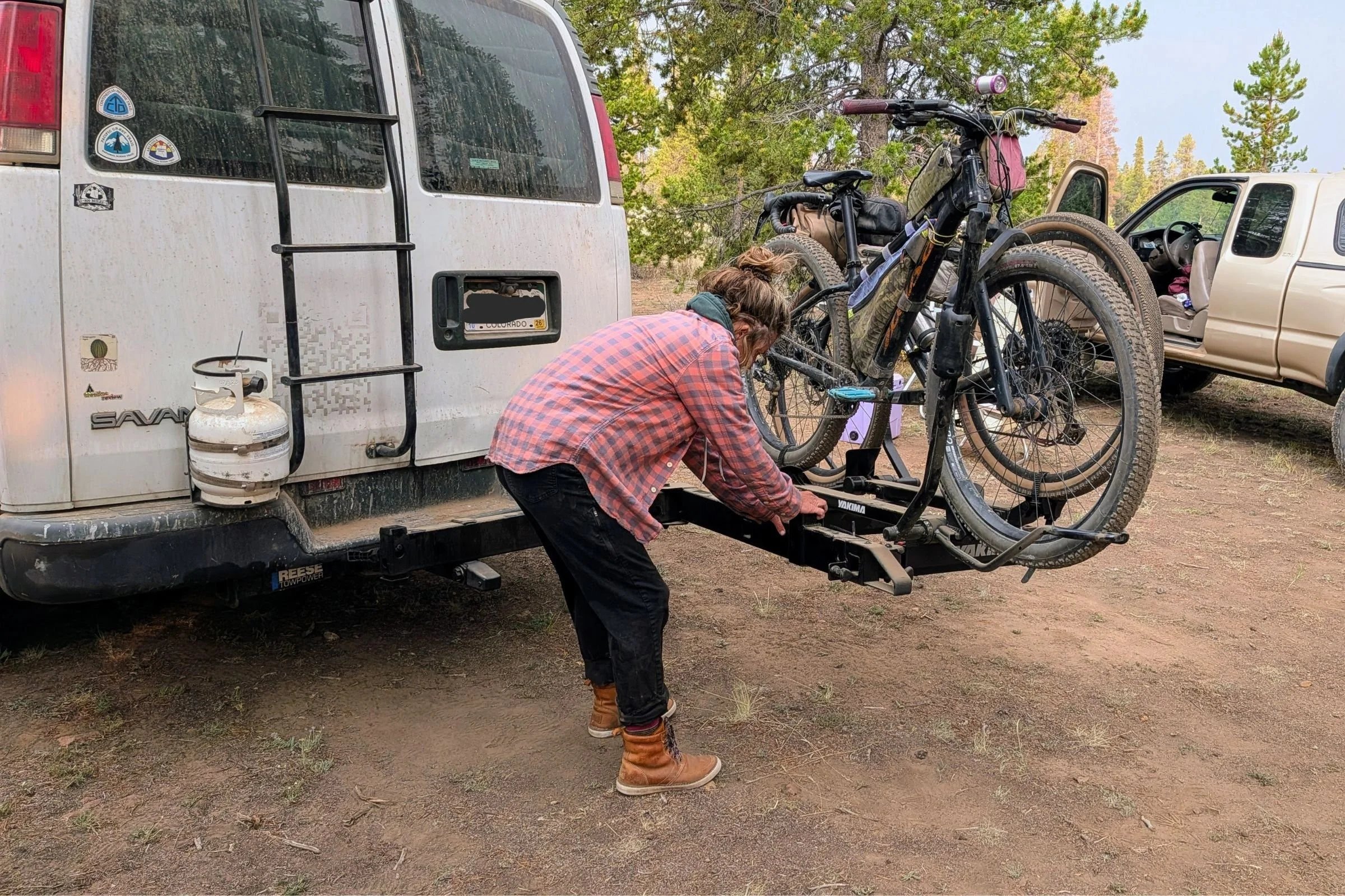 A person loads a bike onto a Yakima EXO DoubleUp 2-Bike Hitch Rack mounted on a trailer.
