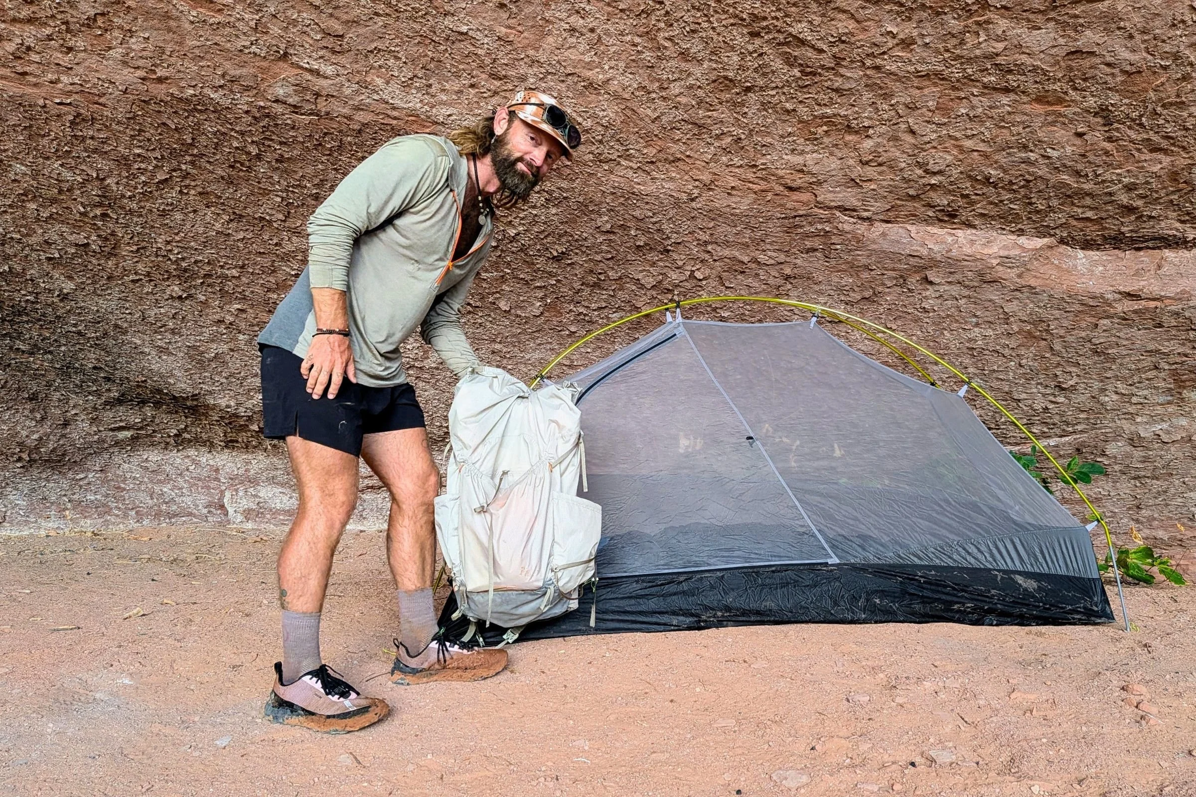 Sam Schild stands with a backpack beside a Gossamer Gear The Free at a rocky campsite.
